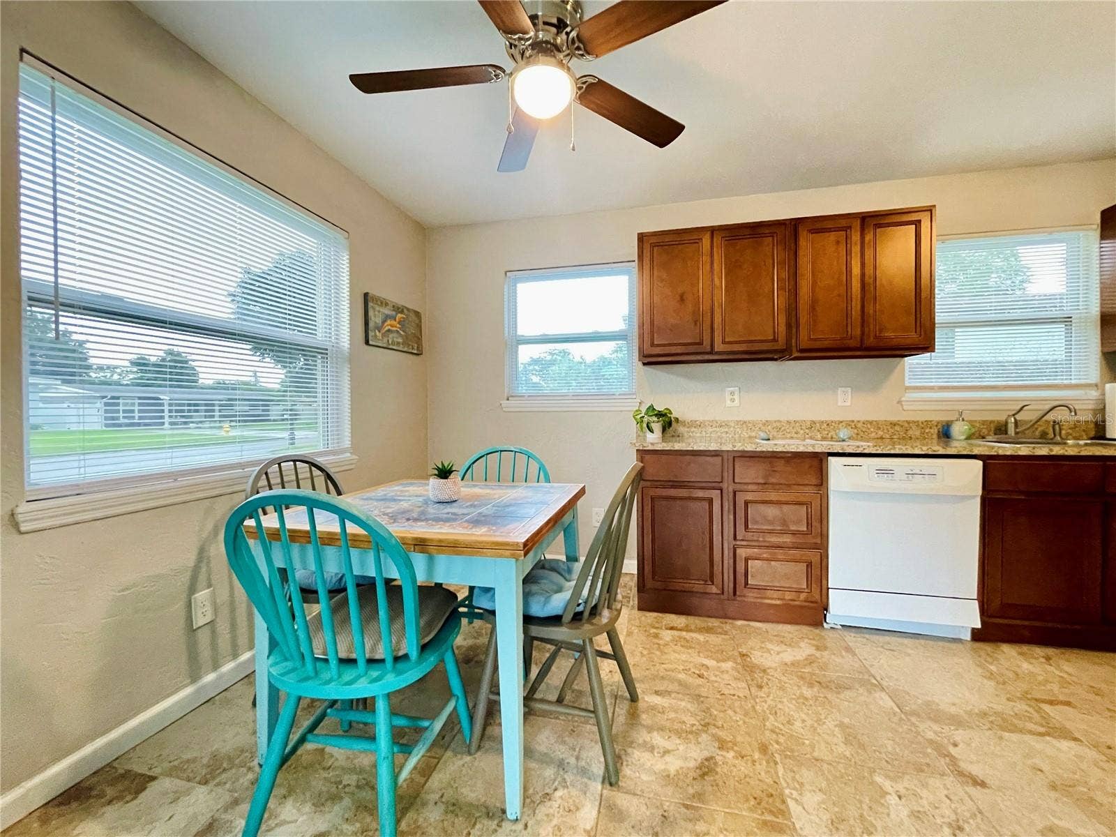 Charming dining niche featuring a vibrant blue table setup tucked next to an expansive kitchen counter with warm wood cabinetry.