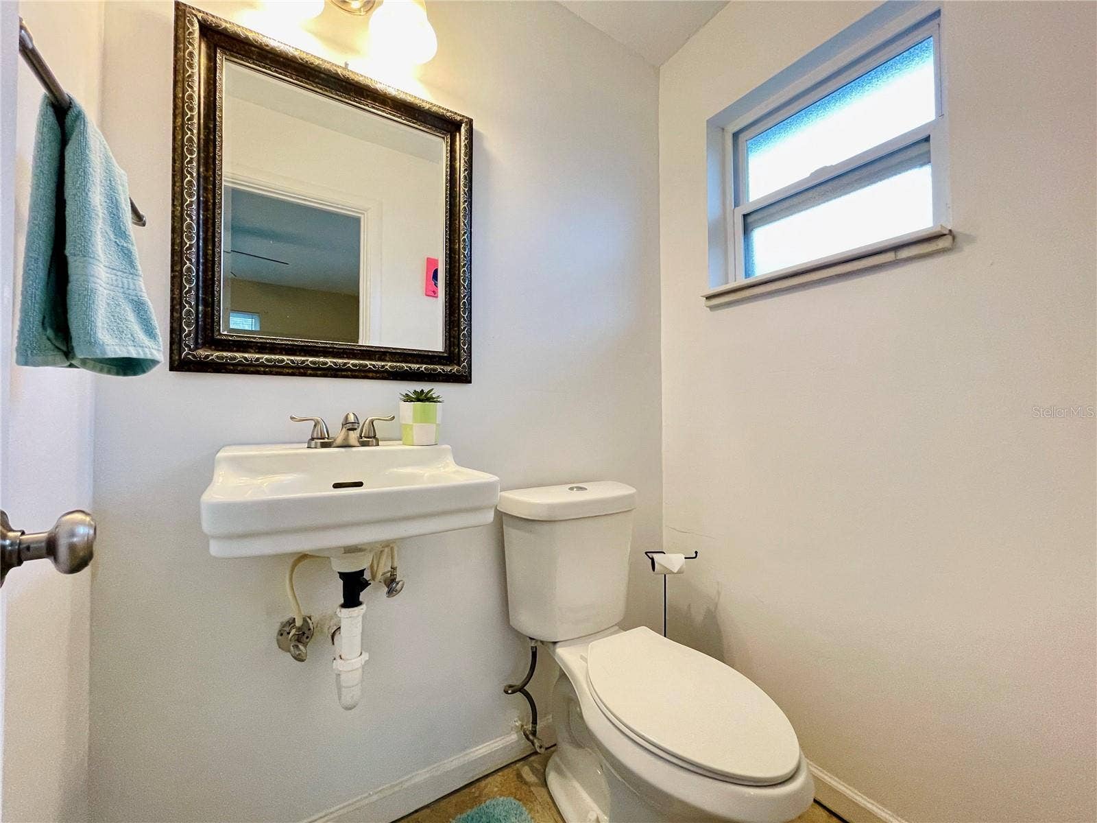 Functional half-bathroom off the bedroom with equipped with a classic wall-mounted sink, a decorative framed mirror, and a frosted privacy window.