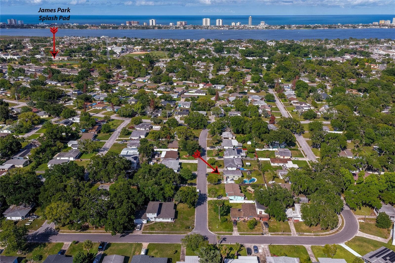 Wide aerial perspective highlighting the propertys location within the neighborhood, with a red arrow pointing toward the home and another local attractions and nearby coastal waters.