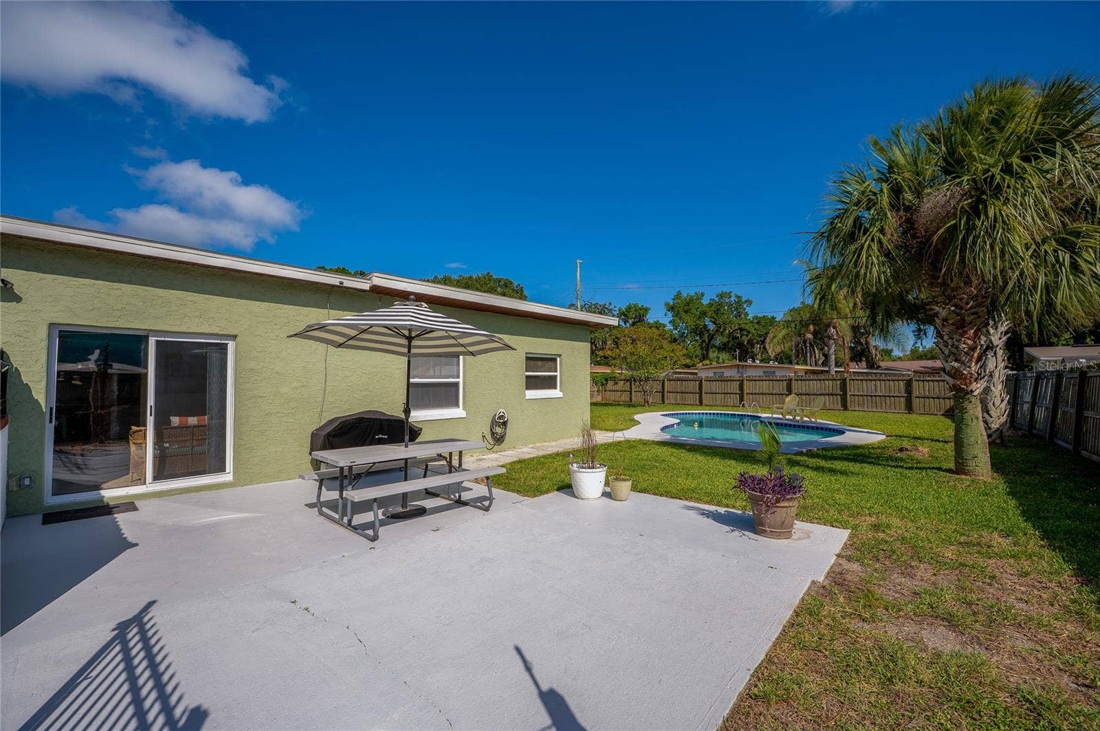 Inviting concrete patio area perfect for outdoor dining, overlooking a spacious green lawn and a private, sparkling in-ground pool.