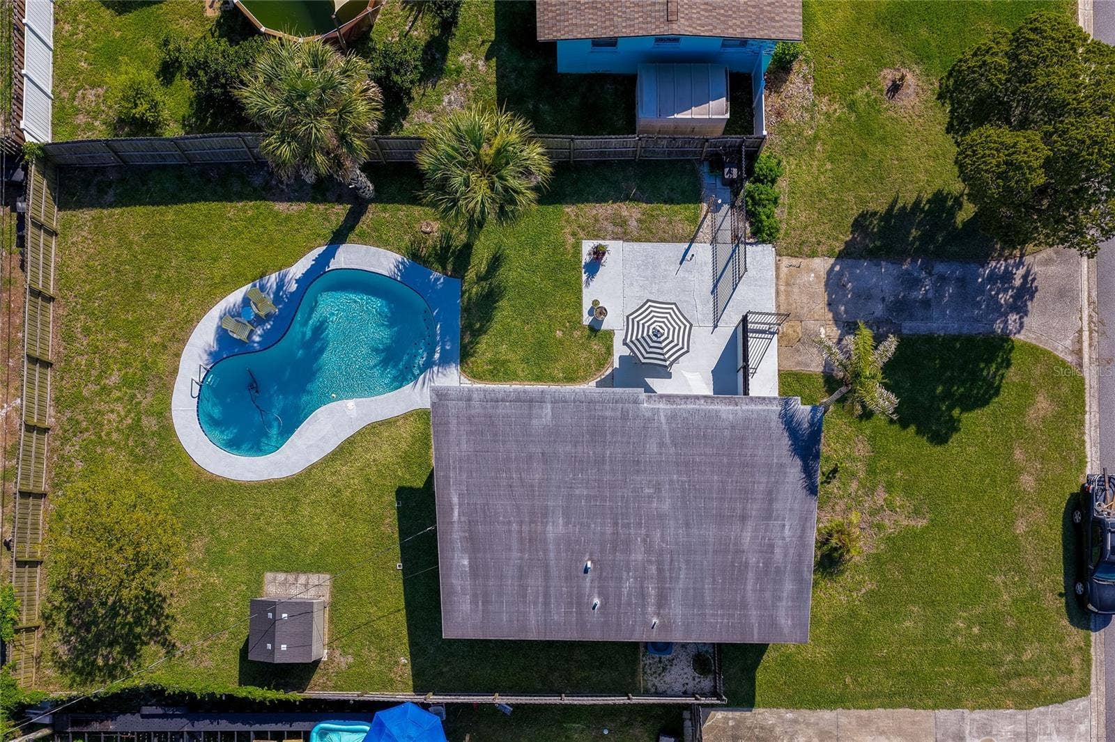Direct top-down aerial view detailing the property's layout, including the homes roof, a paved patio with a seating area, an immaculate lawn, and a swimming pool.
