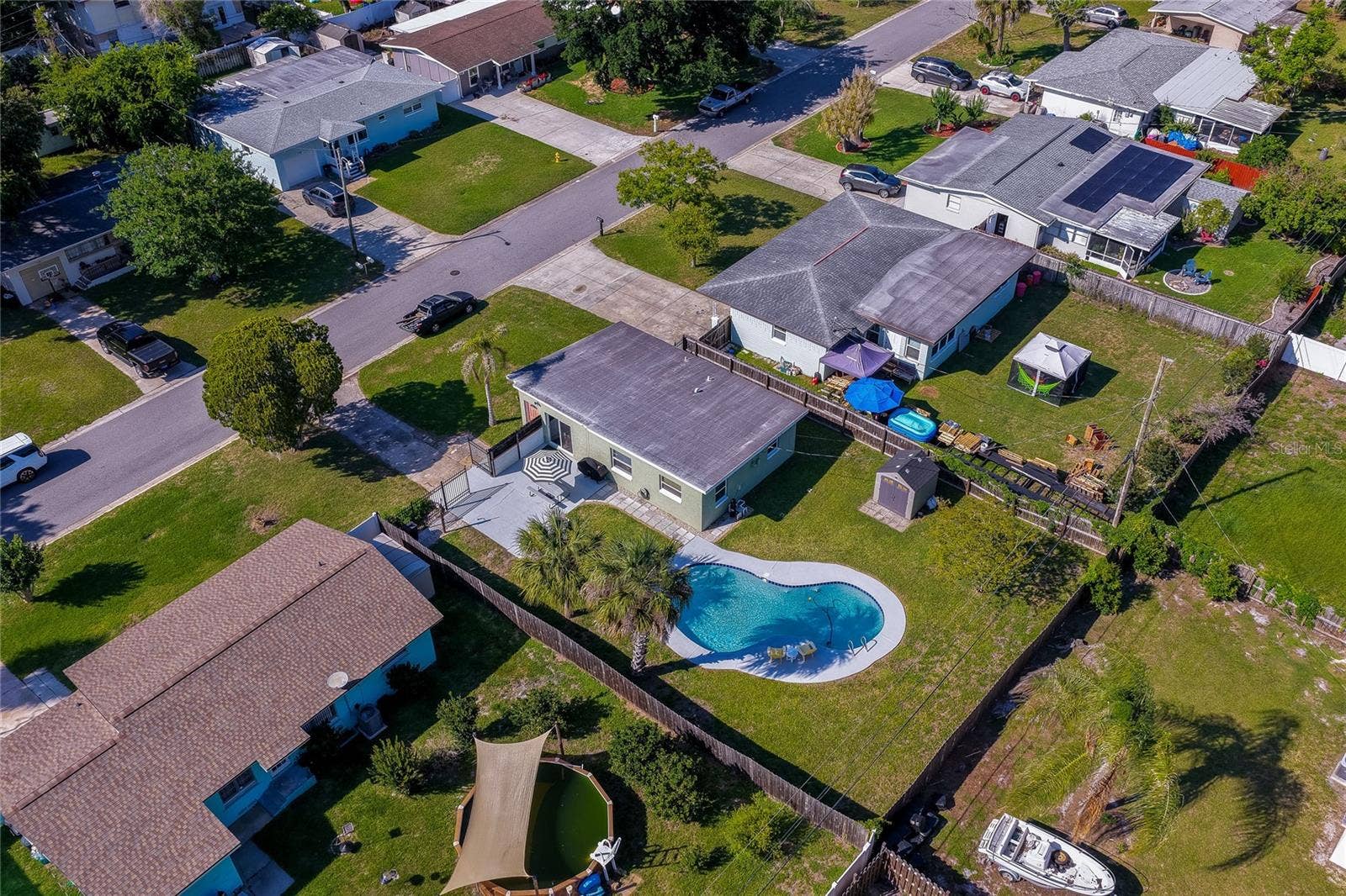 High-angle backyard aerial view capturing the homes gated patio area, detached storage shed, privacy fencing, and refreshing pool.