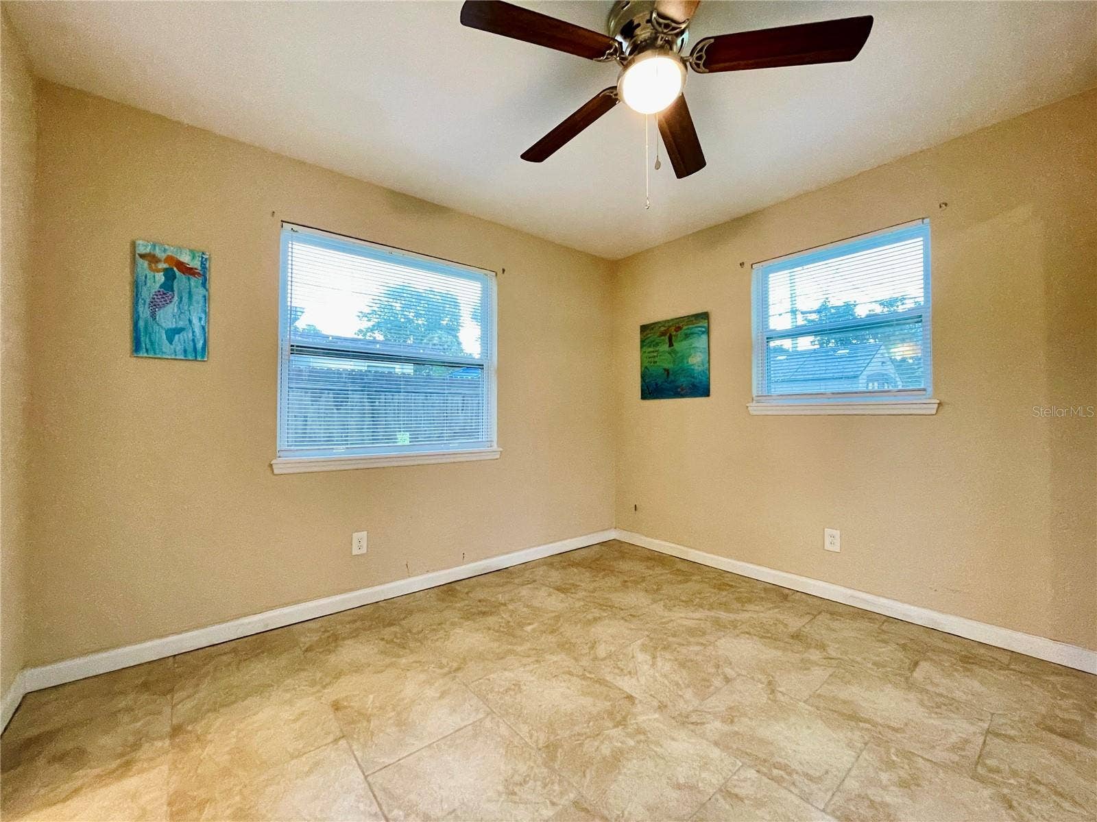 Cozy bedroom featuring warm tan walls, tile flooring, and ample natural light from two windows.