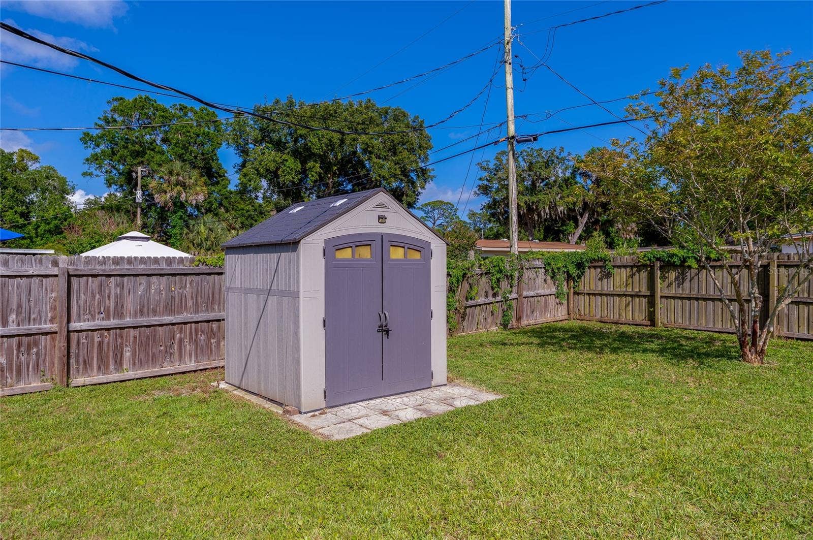 Fully fenced backyard featuring a spacious, modern storage shed set on a paved foundation.
