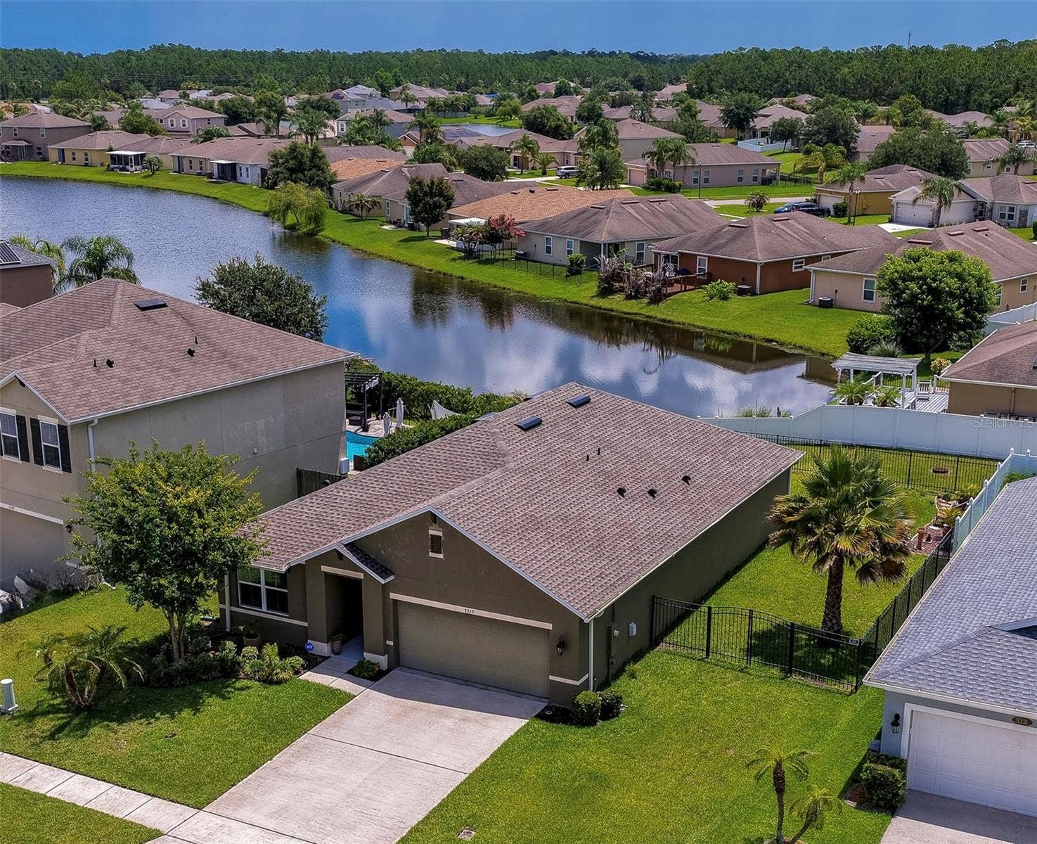 5329 ROYAL PLANTATION BOULEVARD, Port Orange, FL 32128 An elevated, angled view of a suburban neighborhood showcasing a single-story home with an attached two-car garage. The property is surrounded by a manicured green lawn and sits near a scenic neighborhood pond.