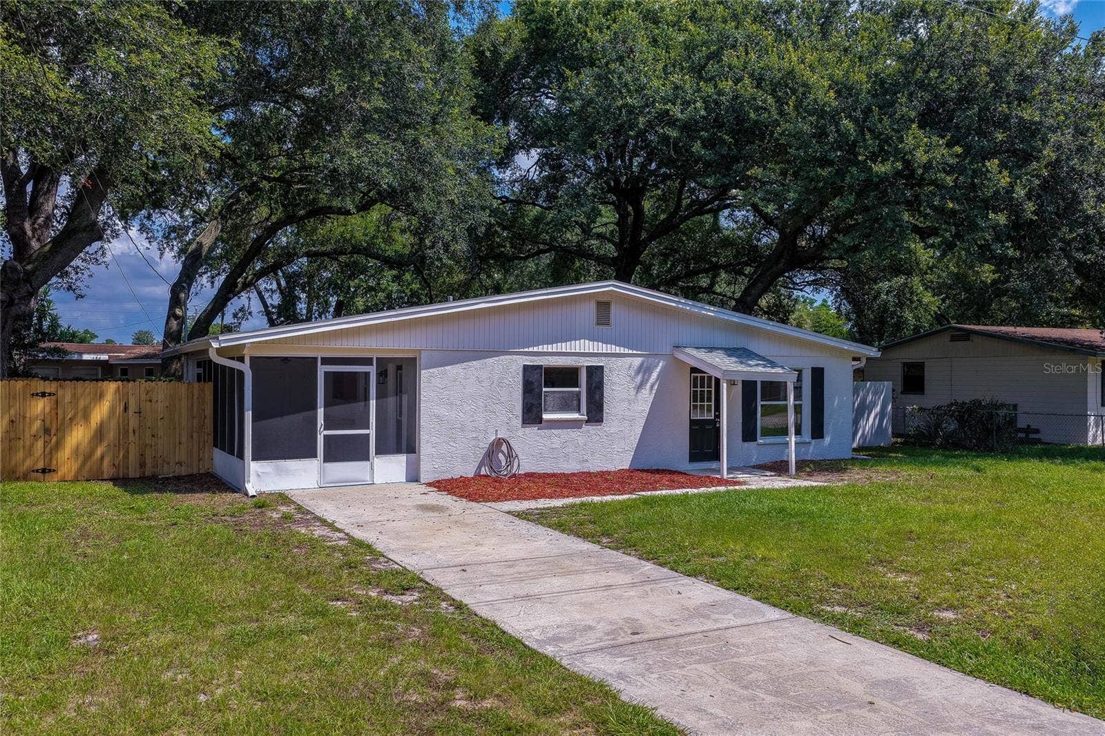 1220 LEON LANE, Daytona Beach, FL 32117 Attractive front elevation featuring fresh exterior finishes, mature oak trees, screened front porch, and welcoming curb appeal.