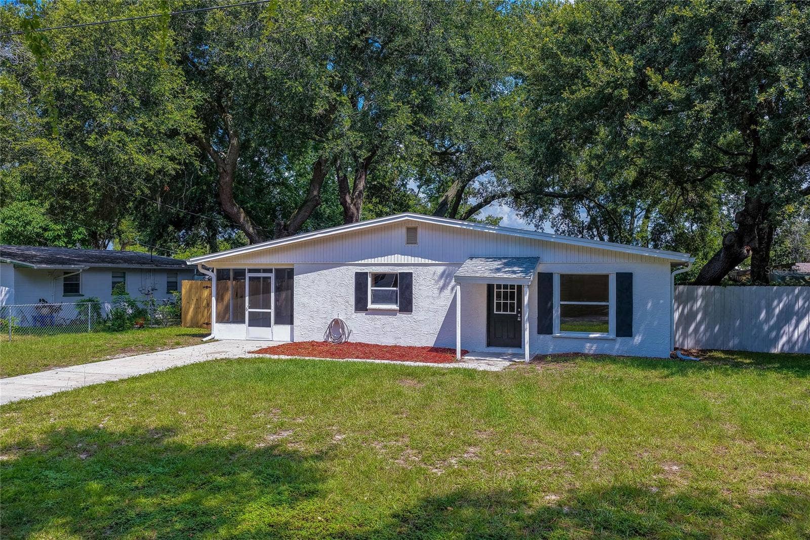 1220 LEON LANE, Daytona Beach, FL 32117 Charming front elevation featuring fresh exterior finishes, a covered entry, screened porch, and mature shade trees that enhance curb appeal.