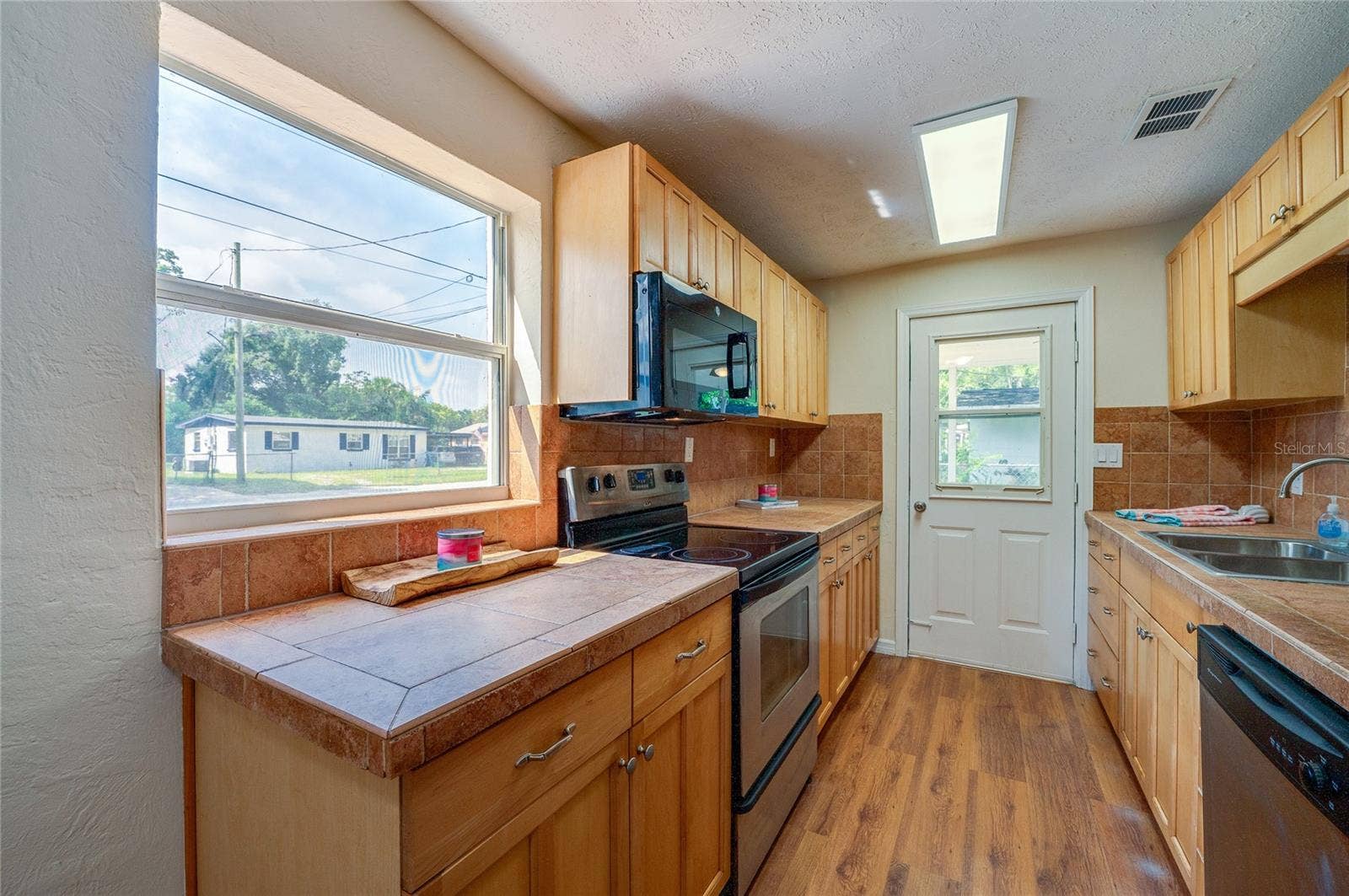 1220 LEON LANE, Daytona Beach, FL 32117 Galley-style kitchen offers generous cabinetry, ample counter space, full appliance package, tile backsplash, and a convenient entry to the screened porch.