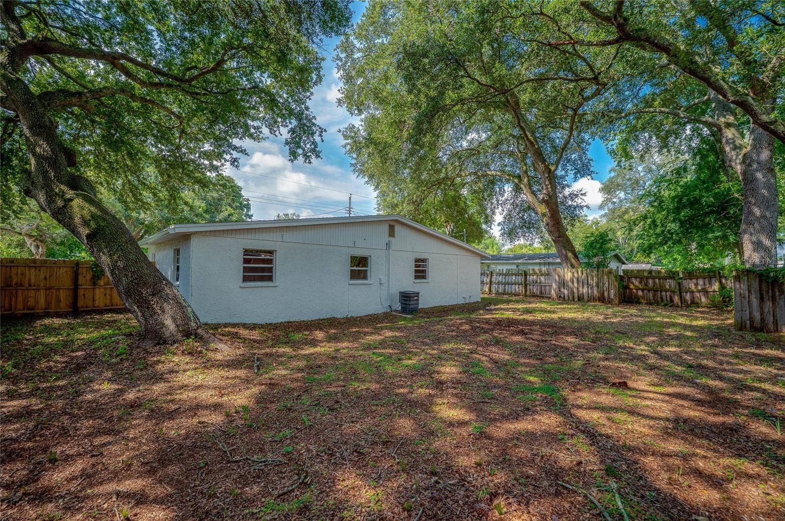 1220 LEON LANE, Daytona Beach, FL 32117 Rear view of the home highlighting the large fenced yard, mature landscaping, and convenient side gate access.