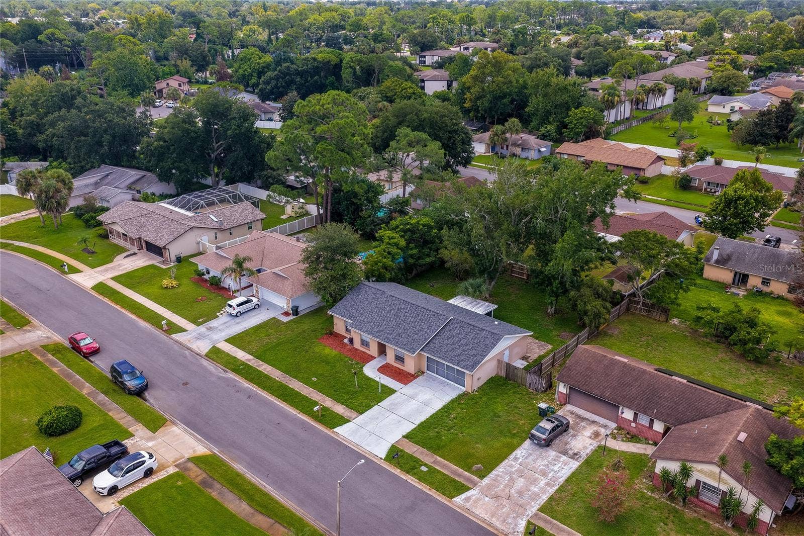 156 SPRINGWOOD DRIVE, Daytona Beach, FL 32119 Aerial view showcasing the property's location within a quiet, tree-lined neighborhood. The single-story home is highlighted alongside its wide driveway, large lot, and surrounding residential community.