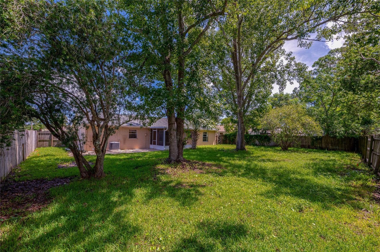 156 SPRINGWOOD DRIVE, Daytona Beach, FL 32119 Expansive green backyard area shaded by large, leafy trees and fully enclosed by a wooden privacy fence. The rear exterior of the single-story home is visible in the background.