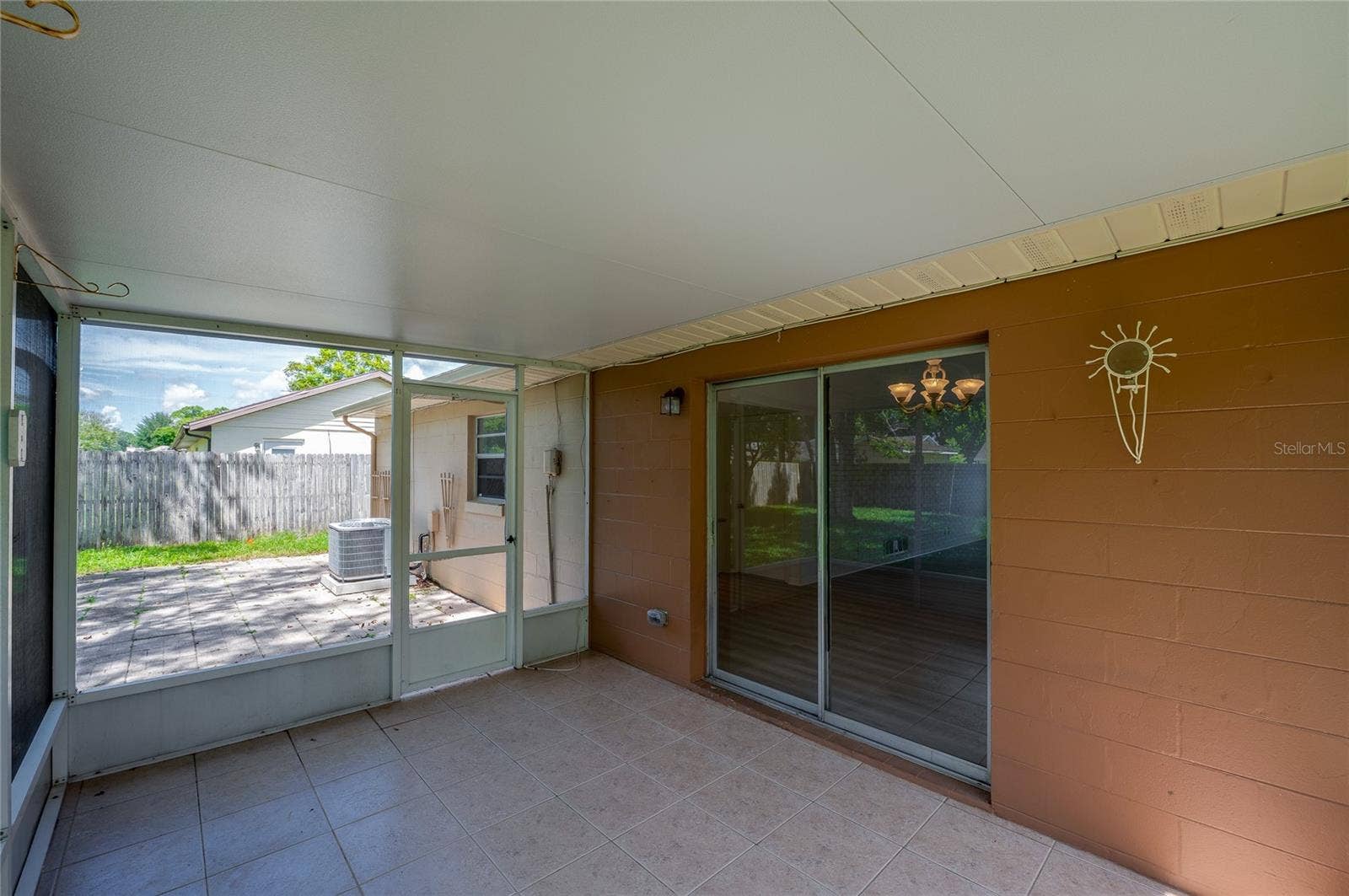 156 SPRINGWOOD DRIVE, Daytona Beach, FL 32119 Covered patio area highlighted by durable tiled flooring, painted block walls, and a sliding glass door providing direct access into the home's interior. A screened door opens out toward an adjacent exterior paved patio space.
