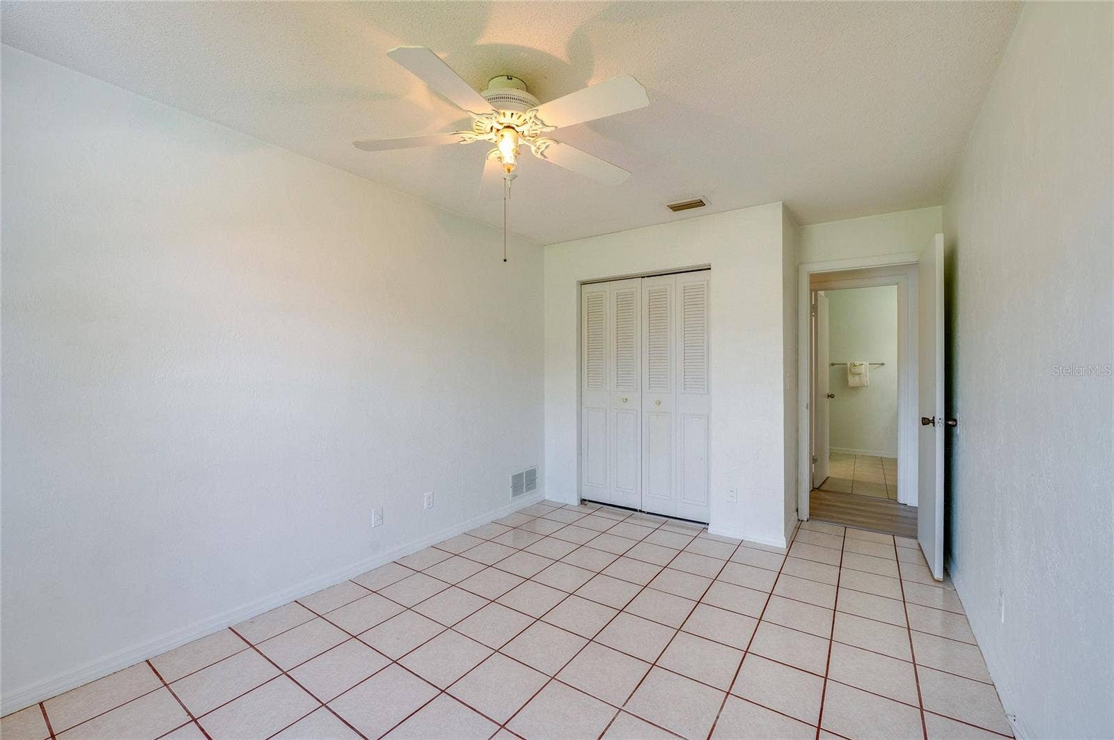 156 SPRINGWOOD DRIVE, Daytona Beach, FL 32119 Clean bedroom space highlighting square tile flooring, neutral paint, and a white ceiling fan. A bi-fold louvered closet door and an adjoining hallway entrance complete the straightforward room layout.