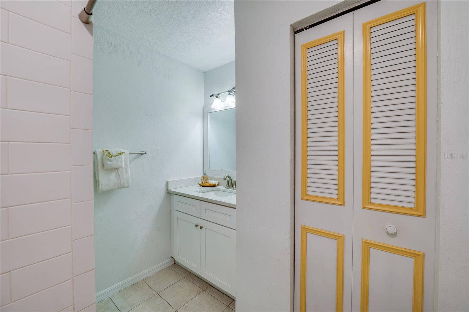 156 SPRINGWOOD DRIVE, Daytona Beach, FL 32119 Updated bathroom space featuring a white vanity with silver hardware, a framed mirror, and bright vanity lighting. Accent bi-fold doors and tile flooring lead into the step-in shower area.