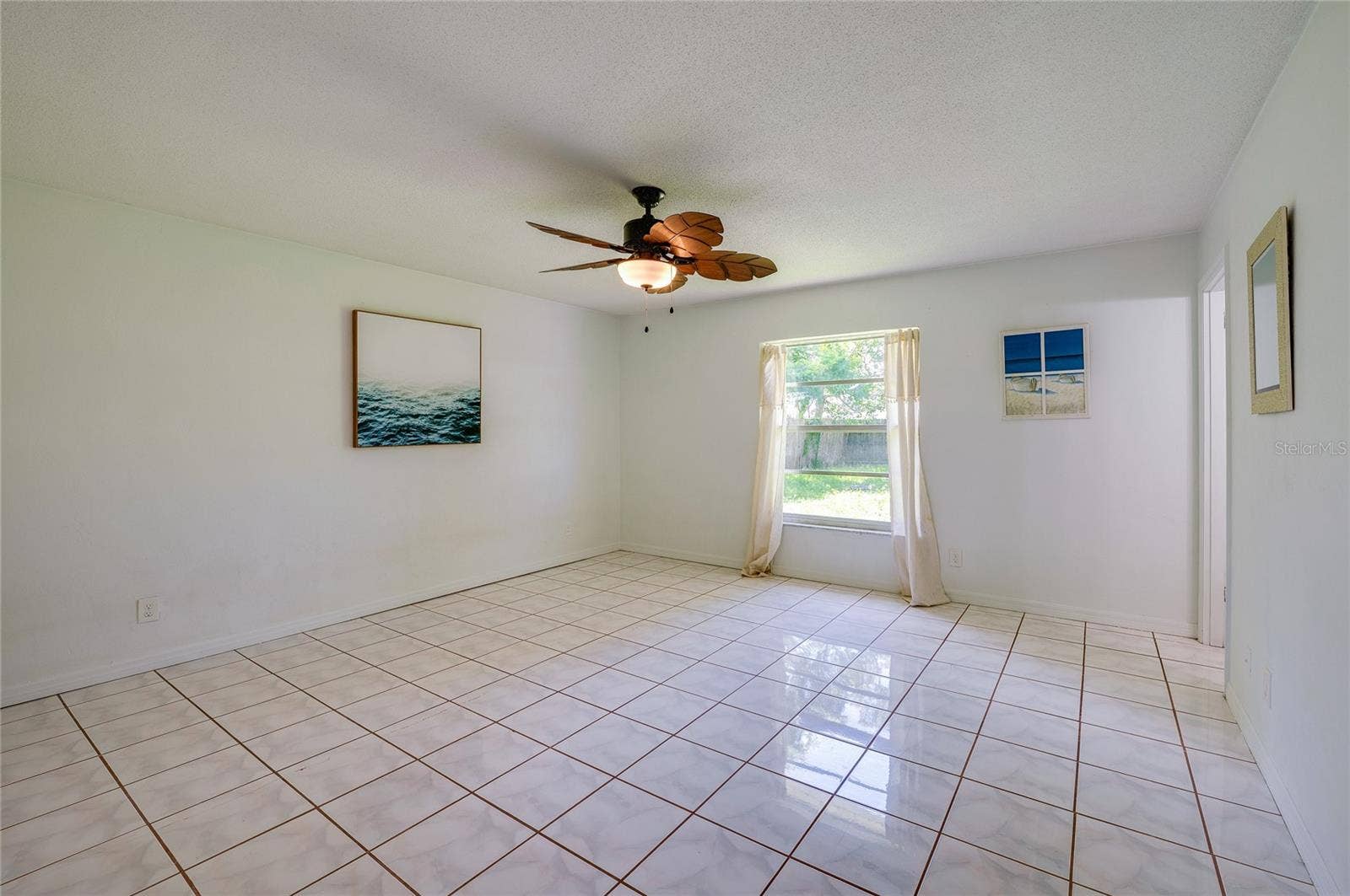 156 SPRINGWOOD DRIVE, Daytona Beach, FL 32119 Generous primary bedroom area featuring glossy tiled flooring, neutral walls, and a tropical-style wooden ceiling fan. A single window brings natural light into the open space.