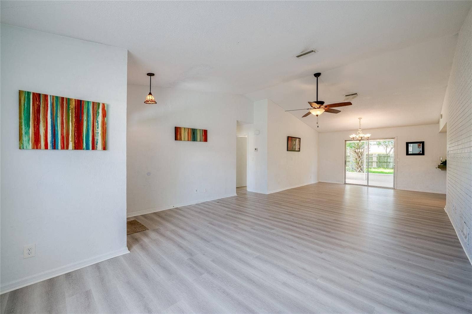 156 SPRINGWOOD DRIVE, Daytona Beach, FL 32119 Bright interior space featuring light luxury vinyl floors, vaulted ceilings, and hanging light fixtures. The open layout seamlessly connects the entry area to the main living and dining spaces.