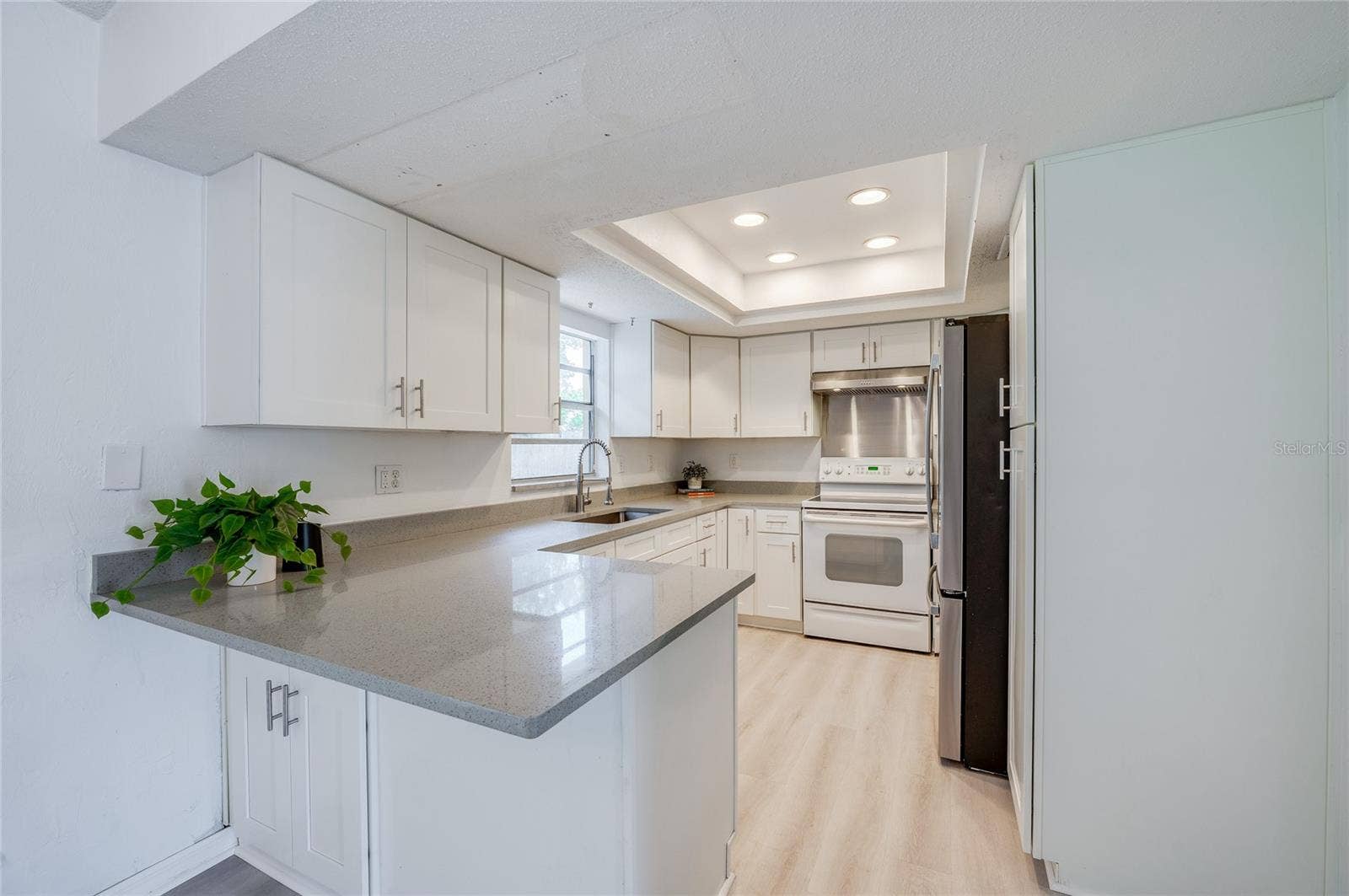 156 SPRINGWOOD DRIVE, Daytona Beach, FL 32119 Modernized kitchen featuring sleek white cabinetry, quartz countertops, and an elevated recessed ceiling with built-in lighting. Stainless steel appliances and a breakfast bar peninsula complete the functional layout.