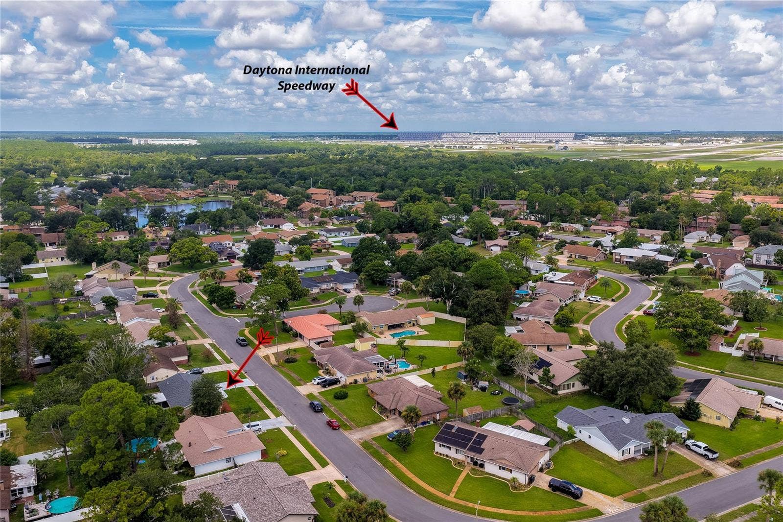 156 SPRINGWOOD DRIVE, Daytona Beach, FL 32119 High-angle aerial view of the surrounding residential neighborhood, pointing out the home's proximity to the nearby Daytona International Speedway. The surrounding area features lush tree-lined streets and well-spaced single-family home lots.