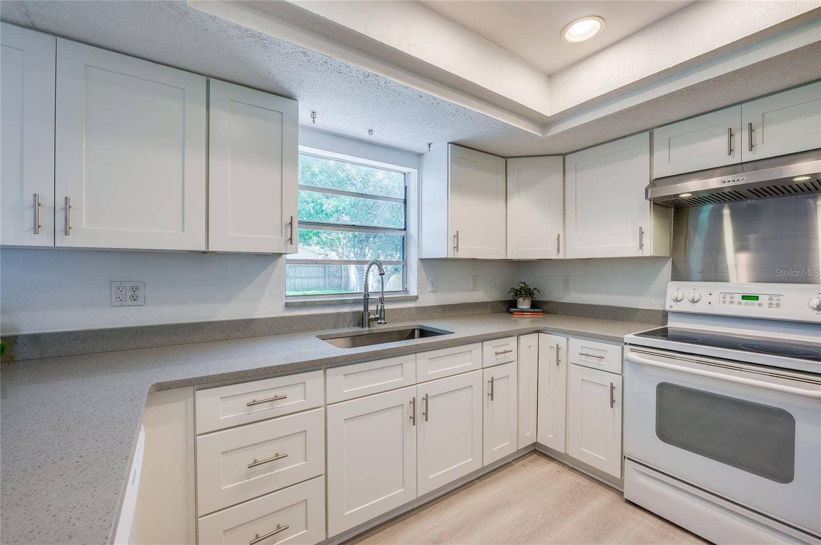 156 SPRINGWOOD DRIVE, Daytona Beach, FL 32119 Well-lit kitchen area offering abundant white cabinetry, durable quartz countertops, and a window overlooking the backyard. A stainless steel range hood, smooth-top stove, and deep sink frame the efficient workflow.