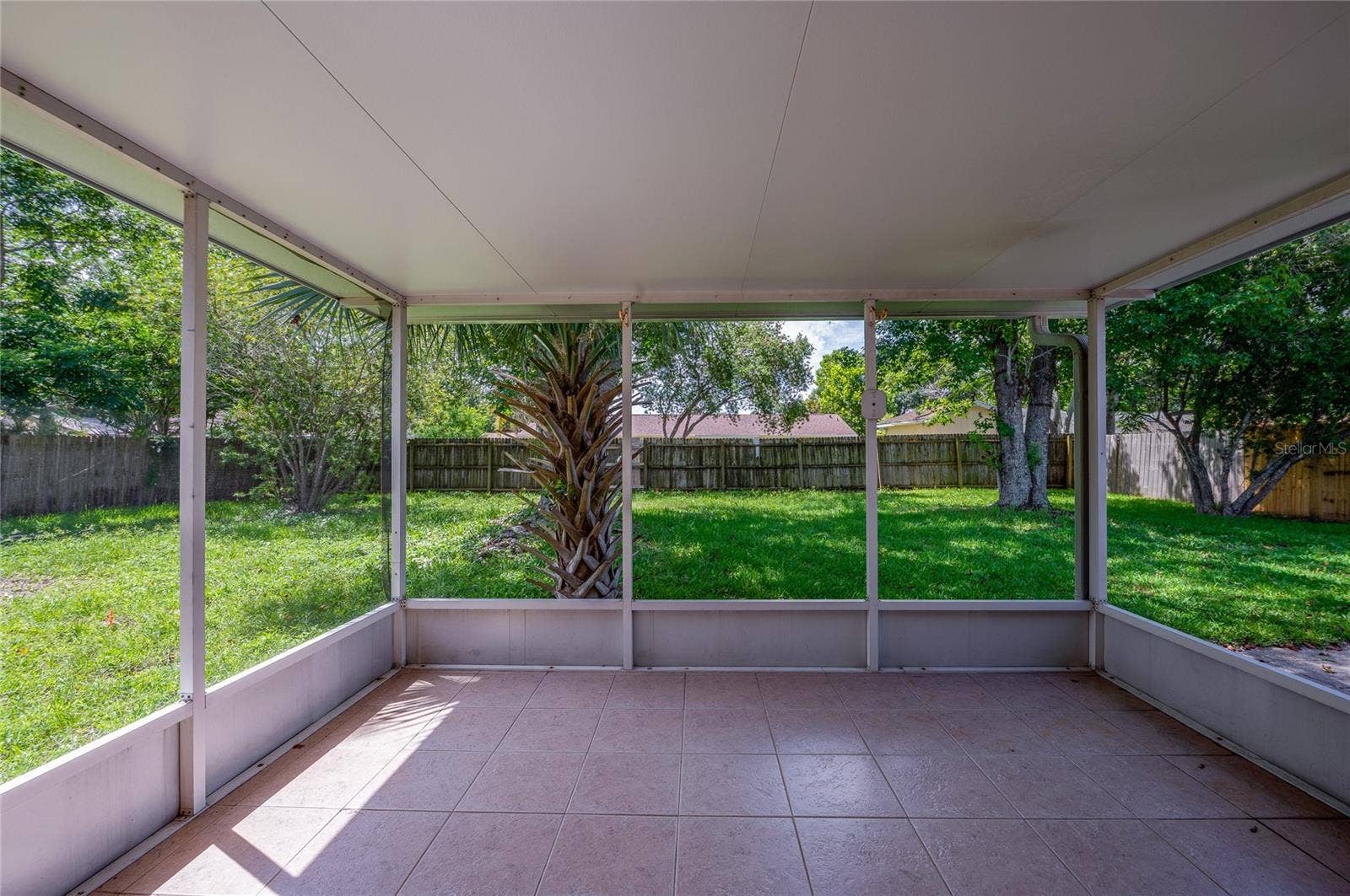 156 SPRINGWOOD DRIVE, Daytona Beach, FL 32119 Enclosed screened porch featuring neutral tile flooring, a solid covered ceiling, and floor-to-ceiling screens overlooking a spacious, grass-covered backyard framed by mature trees and a wooden privacy fence.