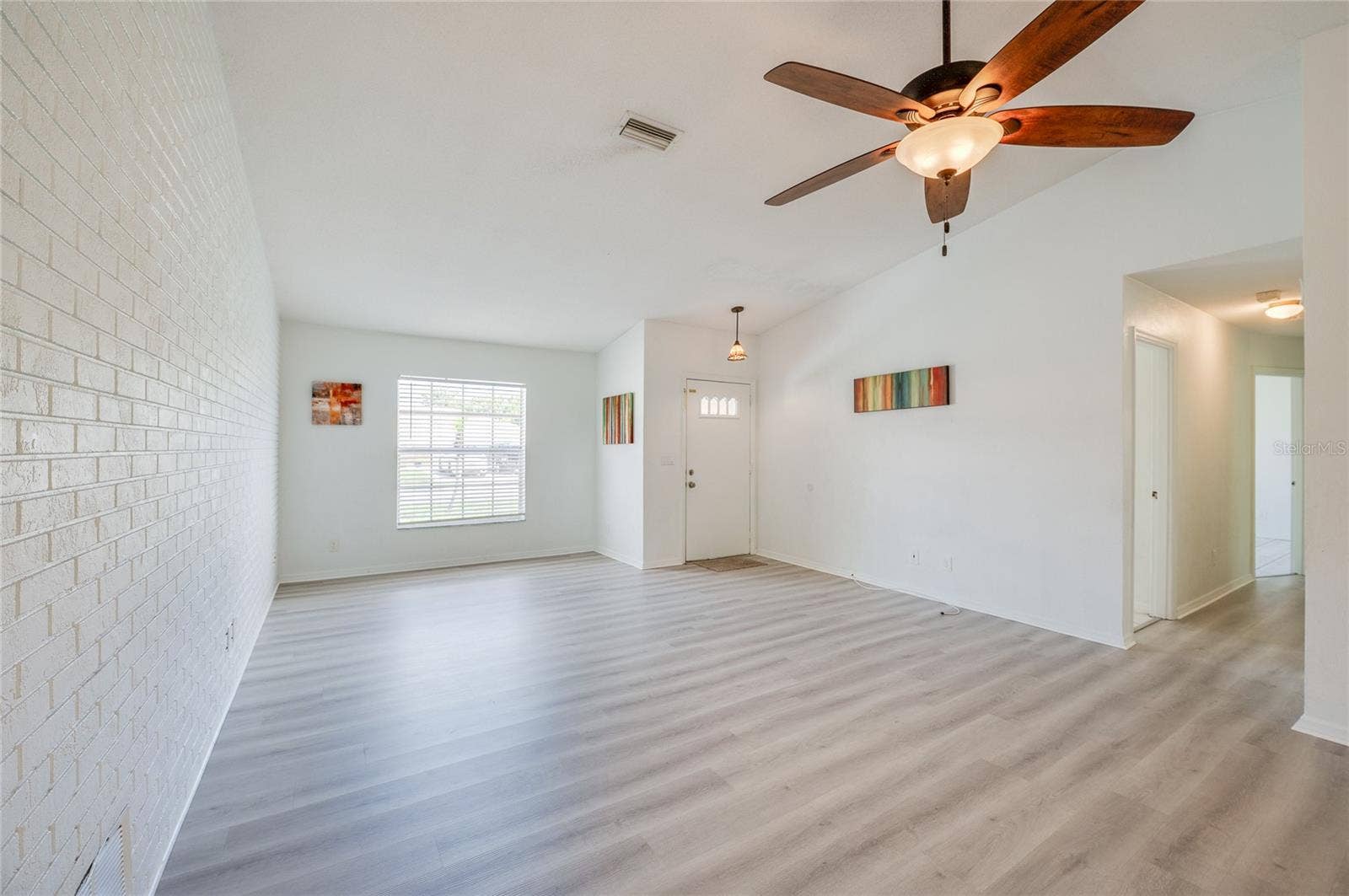 156 SPRINGWOOD DRIVE, Daytona Beach, FL 32119 Welcoming foyer and main living room showcasing white walls, modern luxury vinyl flooring, and a ceiling fan with light fixture. A painted brick accent wall adds character to the functional entryway.