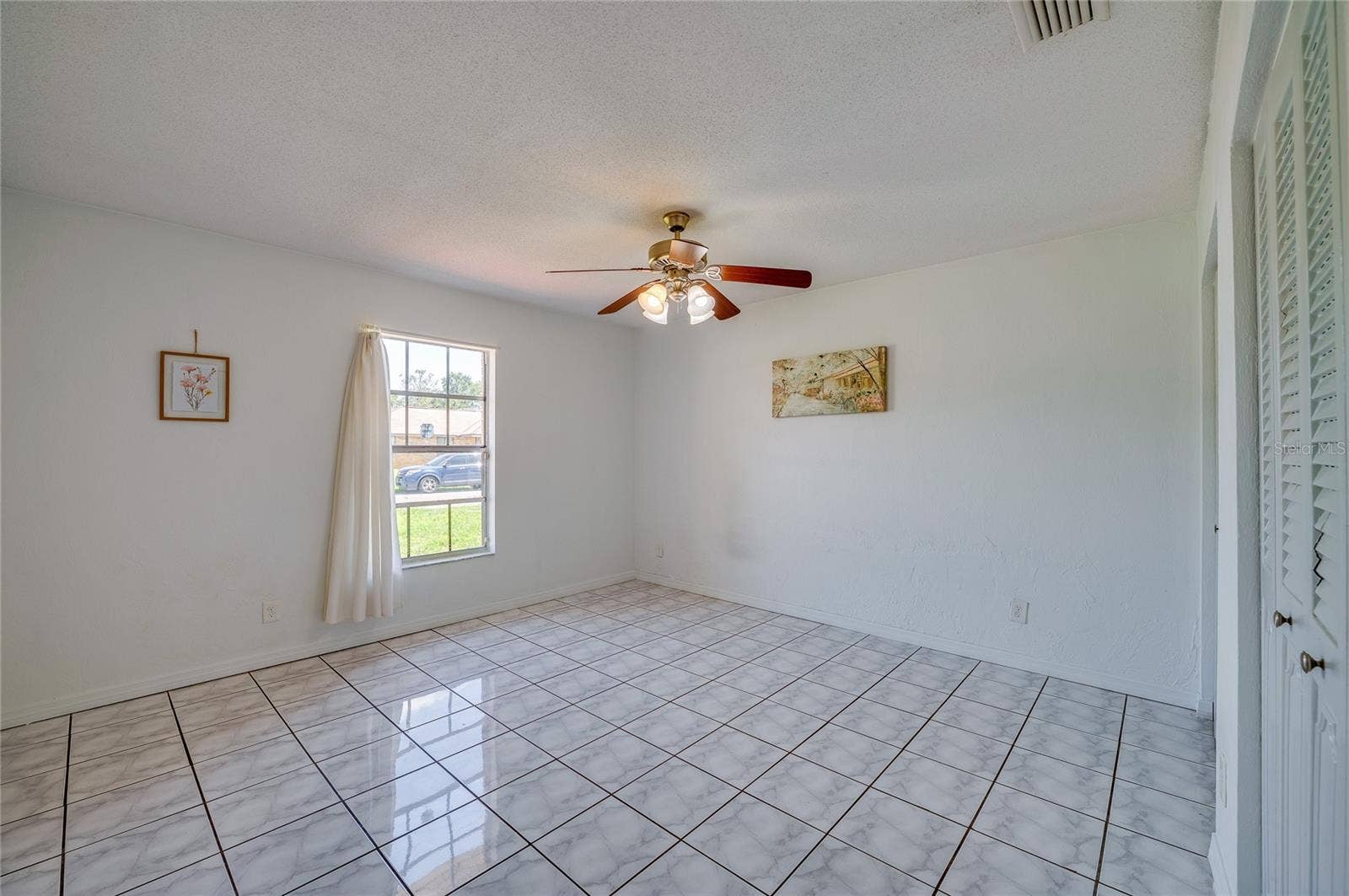 156 SPRINGWOOD DRIVE, Daytona Beach, FL 32119 Spacious interior room featuring light-toned square tile flooring, neutral walls, and a wooden ceiling fan. A bright window provides natural light and views of the surrounding neighborhood.
