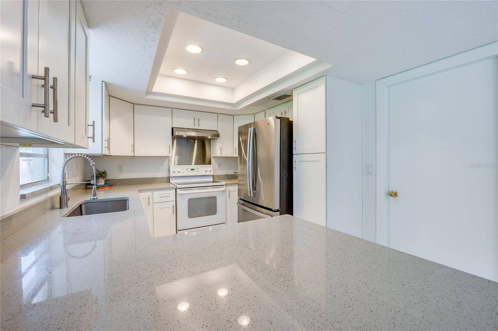 156 SPRINGWOOD DRIVE, Daytona Beach, FL 32119 Bright kitchen layout highlighted by a tray ceiling with inset lighting, ample counter space, and crisp white shaker cabinets. Stainless steel appliances, an undermount sink, and a high-arc faucet offer sleek modern functionality.