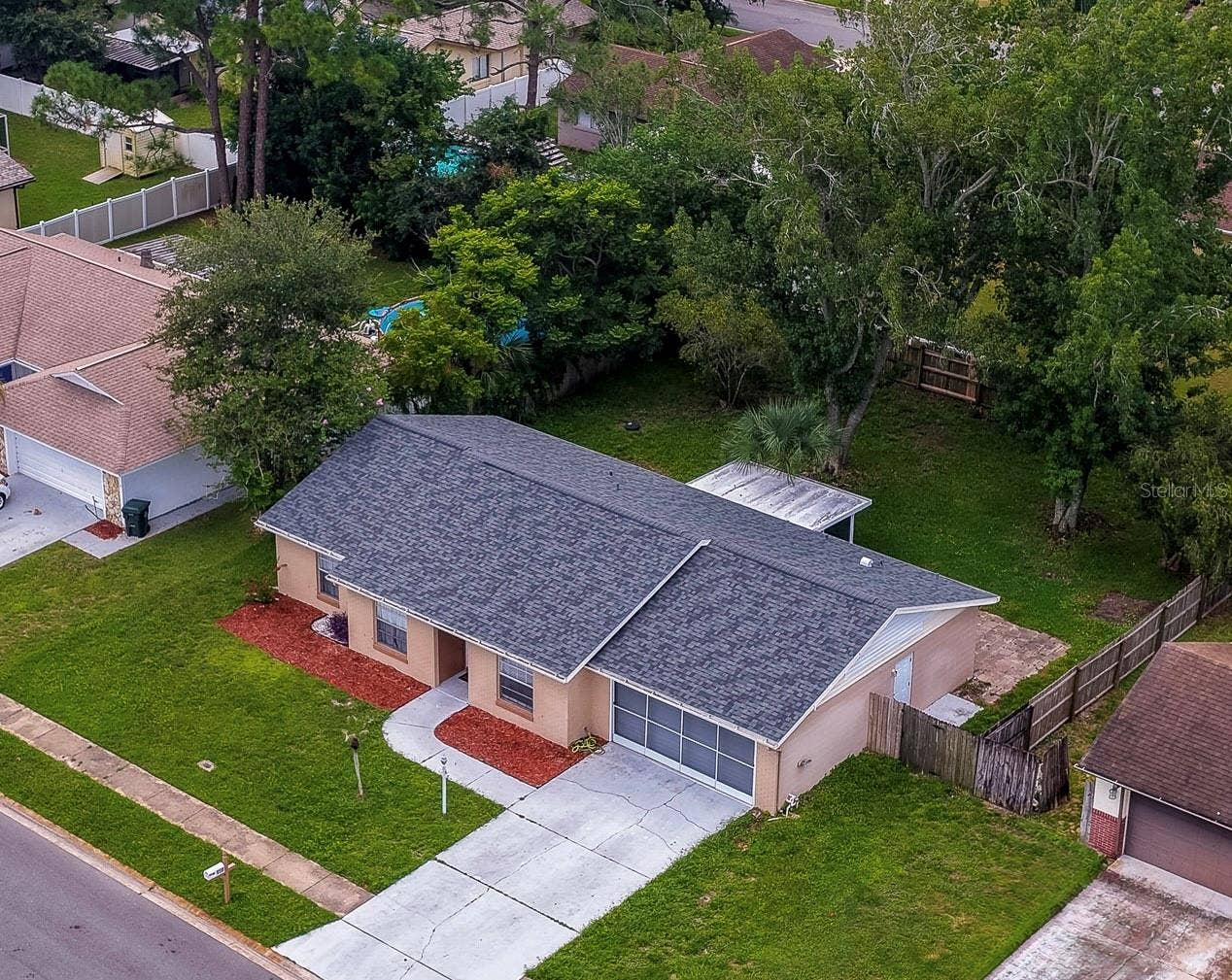 156 SPRINGWOOD DRIVE, Daytona Beach, FL 32119 Elevated perspective of the single-story residence showing a long front walkway, dark roof shingles, and vibrant red mulch landscaping. The property features an expansive front yard bordering a quiet residential street.