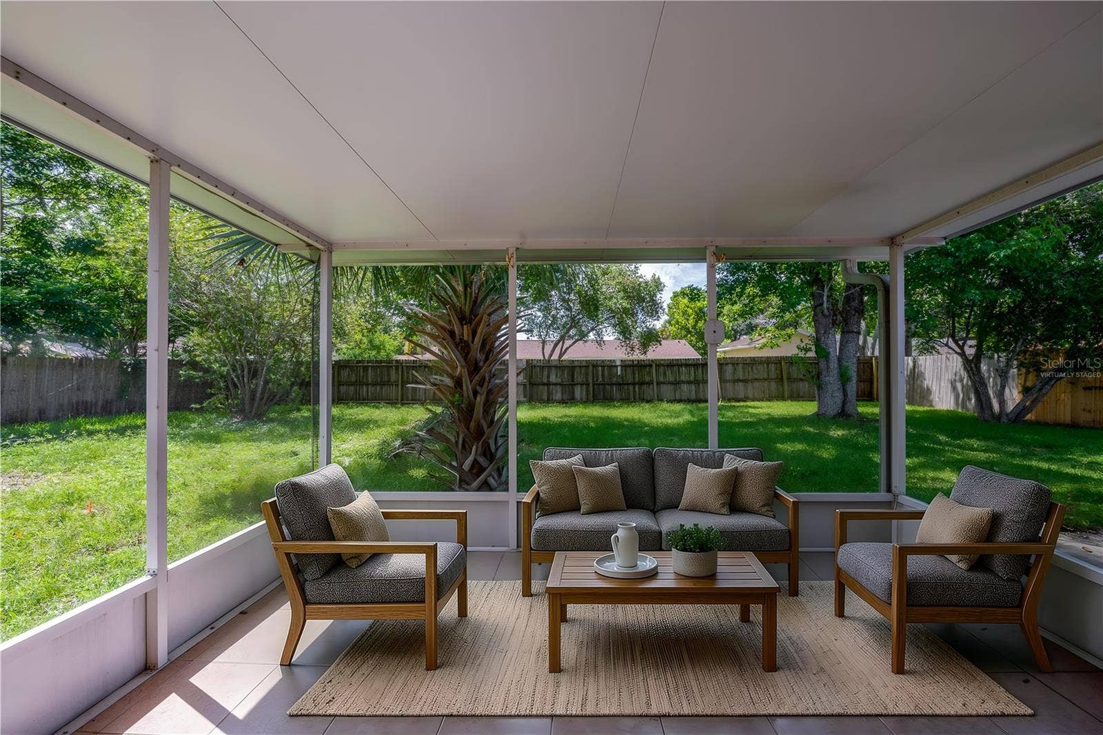 156 SPRINGWOOD DRIVE, Daytona Beach, FL 32119 Virtually Staged. Enclosed screened porch featuring neutral tile flooring, a solid covered ceiling, and floor-to-ceiling screens overlooking a spacious, grass-covered backyard framed by mature trees and a wooden privacy fence.