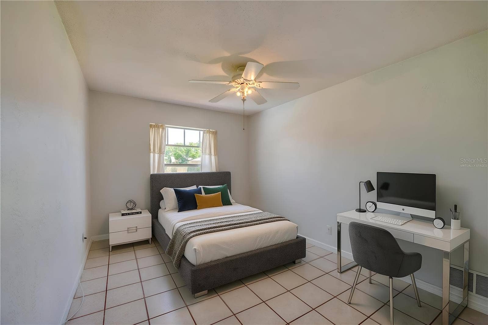 156 SPRINGWOOD DRIVE, Daytona Beach, FL 32119 Virtually Staged. Bright bedroom featuring light-colored tile flooring, neutral walls, and a ceiling fan with light fixture. A single window with curtains lets in natural light while providing views of the outdoors.