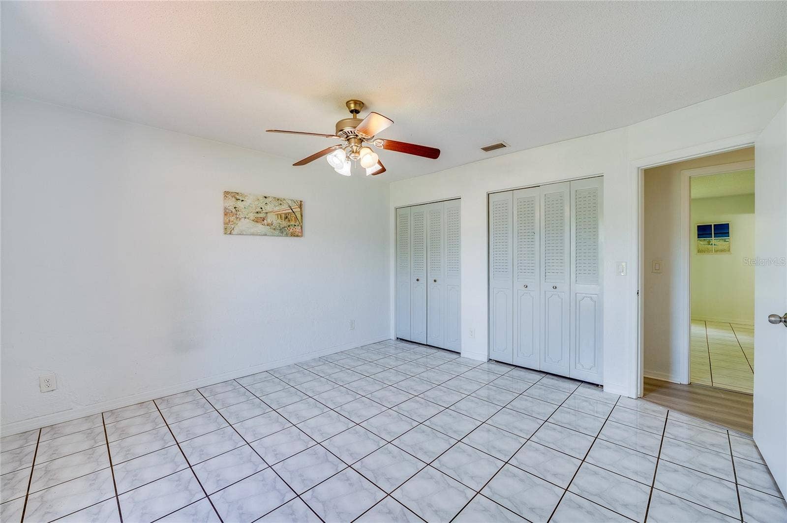 156 SPRINGWOOD DRIVE, Daytona Beach, FL 32119 Well-lit bedroom showcasing tiled floors, crisp white walls, and a central ceiling fan fixture. Two sets of closet doors offer substantial built-in storage along one wall.