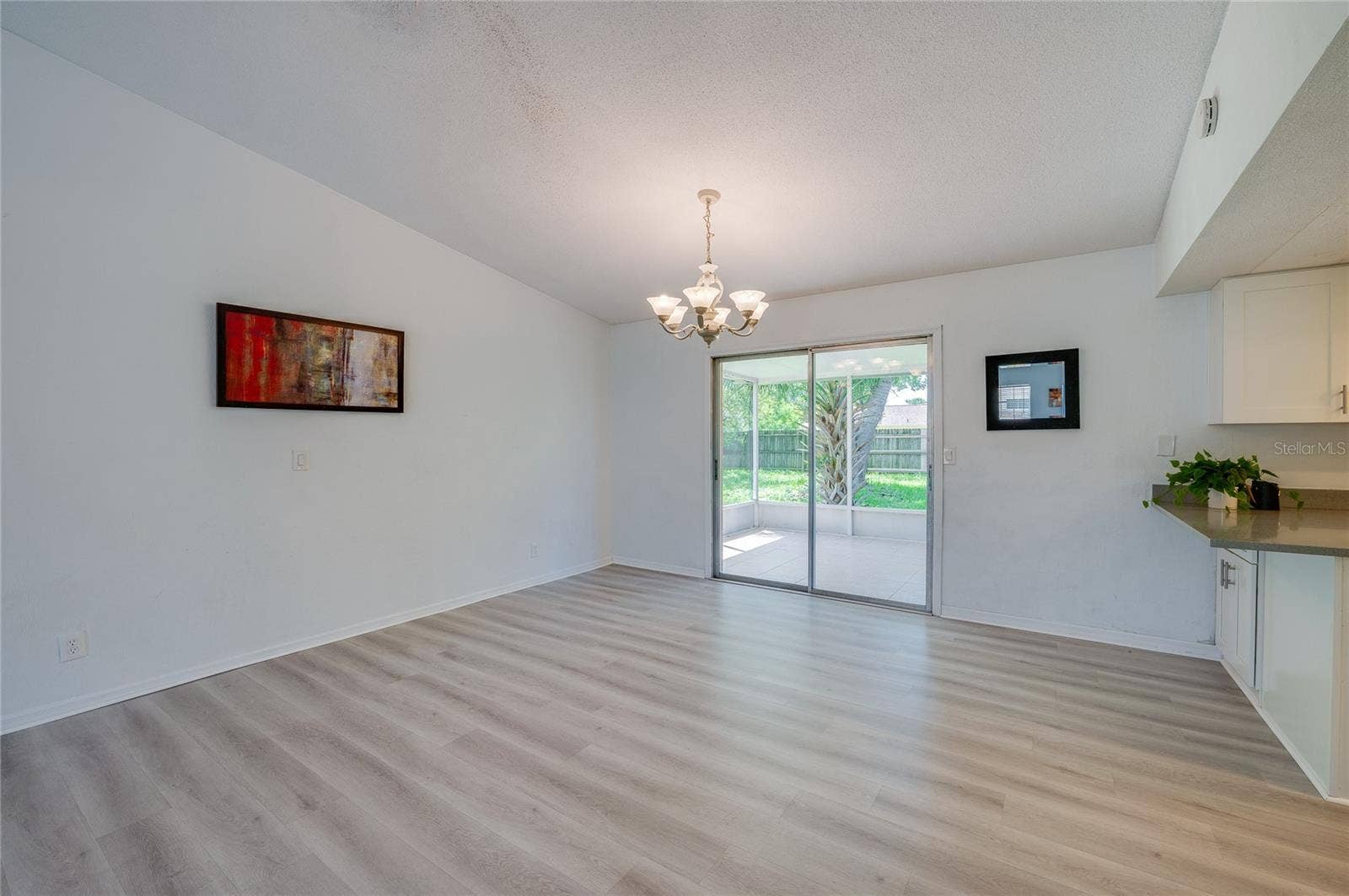 156 SPRINGWOOD DRIVE, Daytona Beach, FL 32119 Inviting dining area featuring an elegant chandelier, light luxury vinyl flooring, and direct access to a screened porch via sliding glass doors. An adjoining counter offers a convenient pass-through connection to the kitchen.