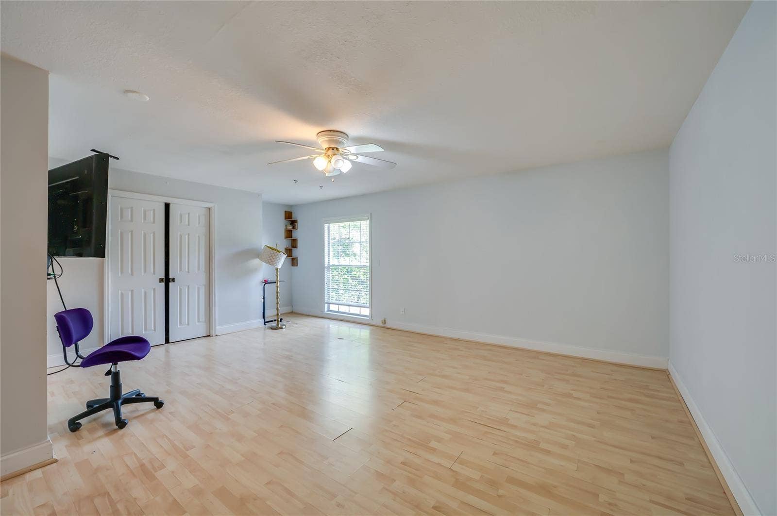 Expansive bedroom room featuring light laminate flooring, soft neutral walls, double-door closet storage, and a large window.
