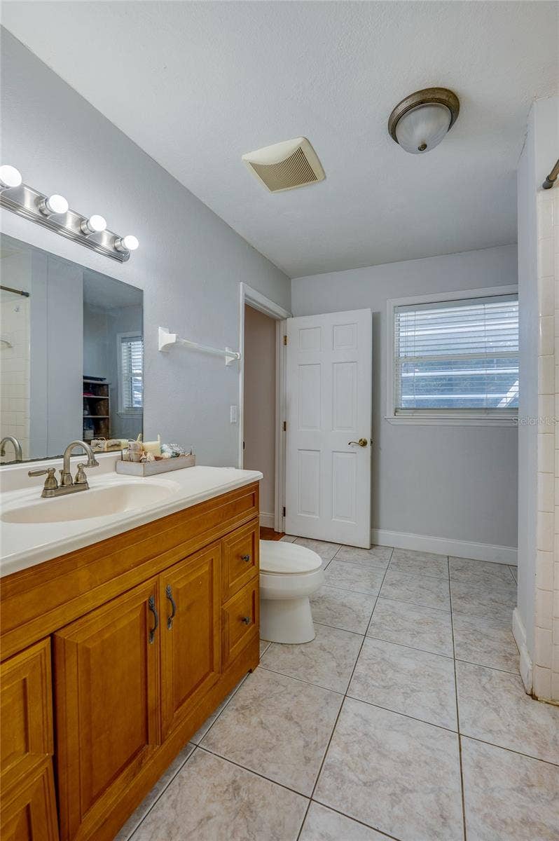 Full bathroom featuring tiled flooring, a warm wood vanity with a large mirror, and light blue walls.