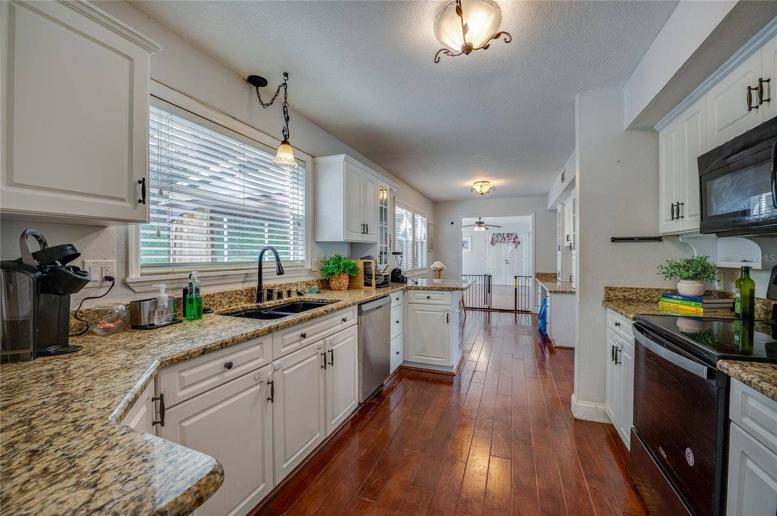 Long galley-style kitchen featuring granite countertops, crisp white cabinets, a black sink basin, and an open sightline through the home.
