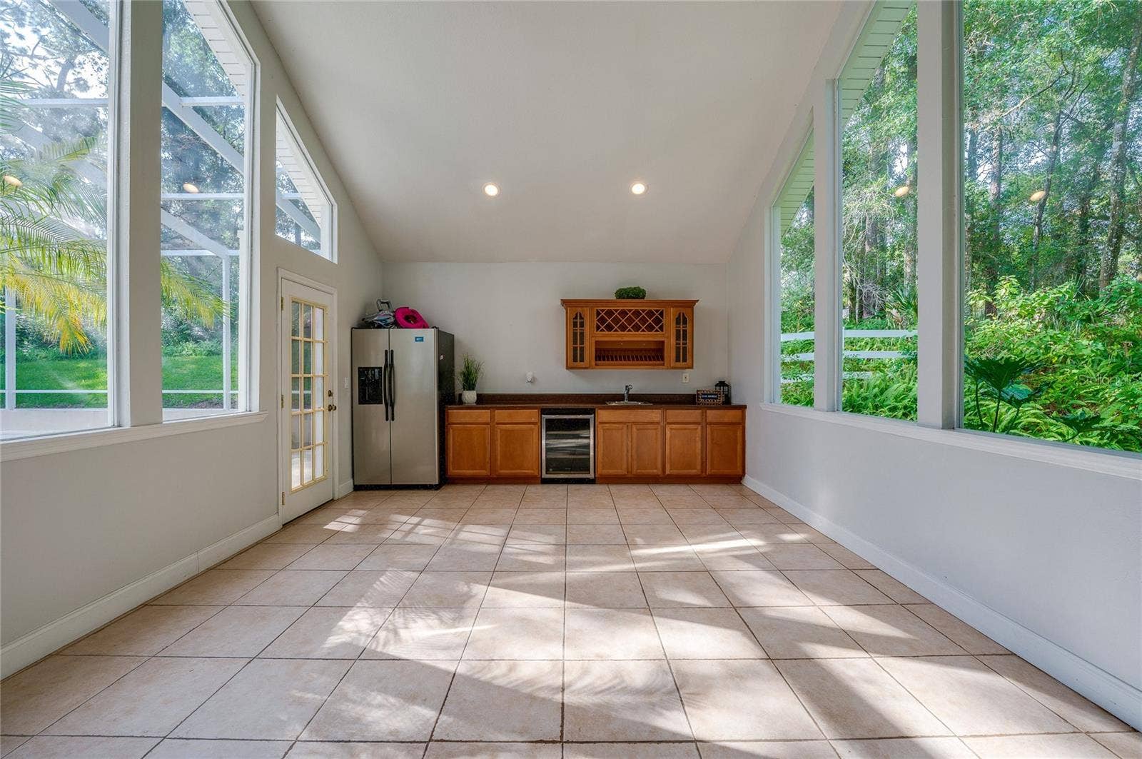 Flex space filled with natural light from floor-to-ceiling windows, featuring tiled floors, vaulted ceilings, and a built-in wet bar setup.
