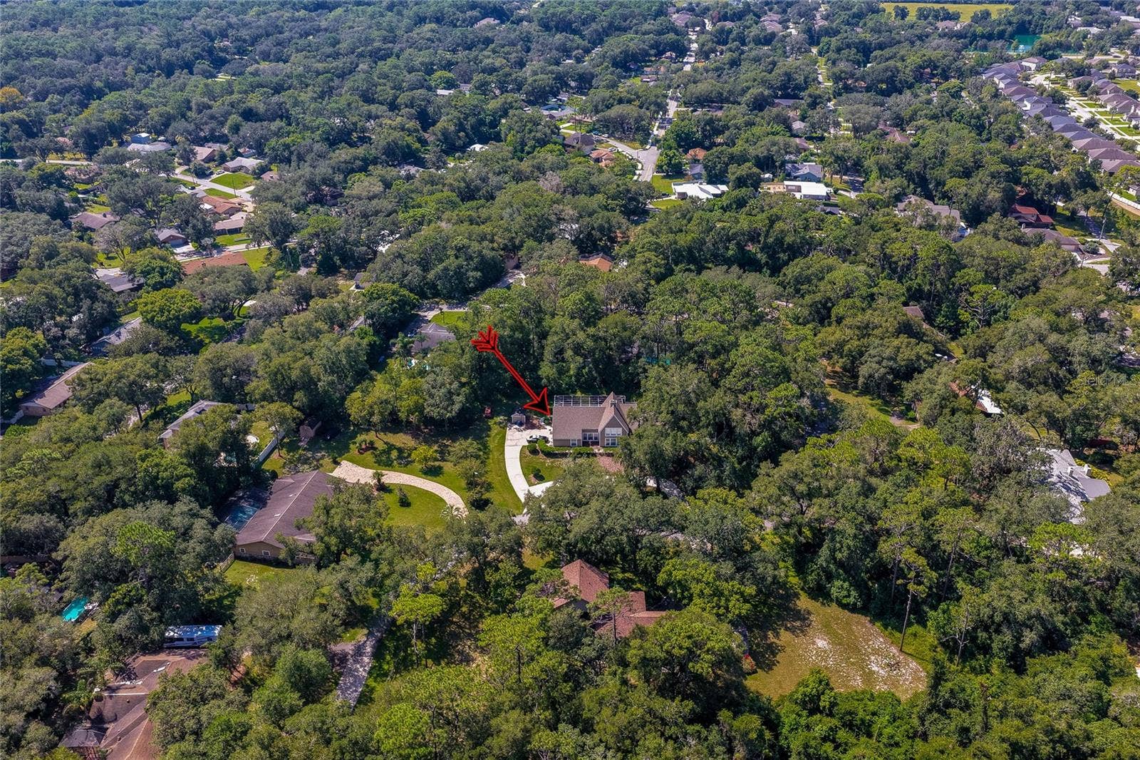 High-altitude aerial shot highlighting the property's location tucked within a lush, tree-filled residential neighborhood.