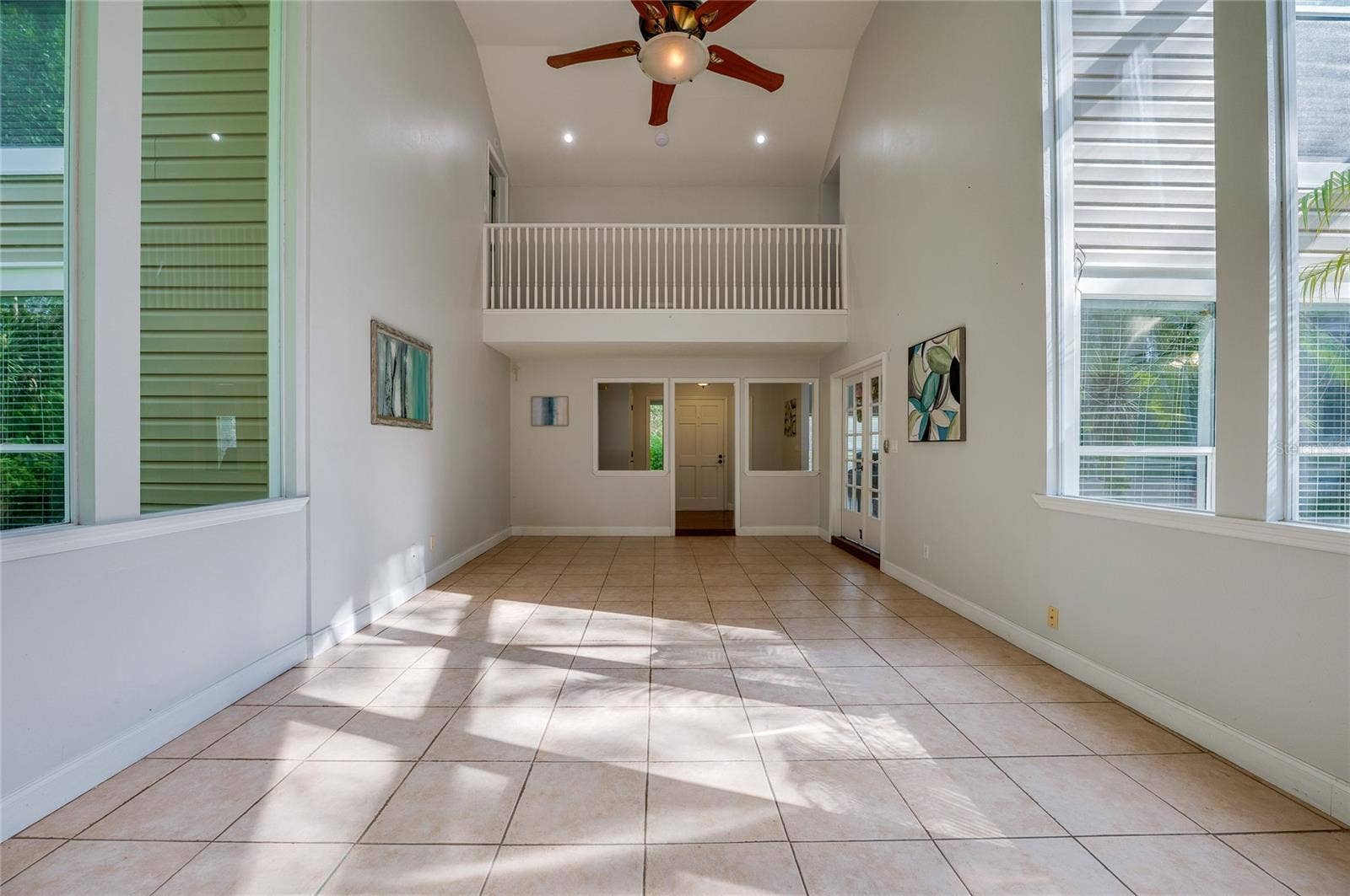 Expansive two-story living area with high ceilings, large windows, tiled flooring, and a overlook balcony on the upper level.