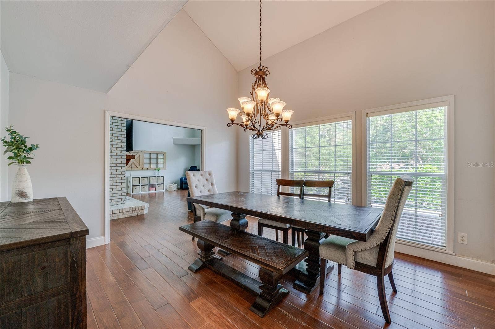Open dining space featuring high ceilings, warm laminate floors, a classic chandelier, and a wide doorway connecting into the adjoining living room.