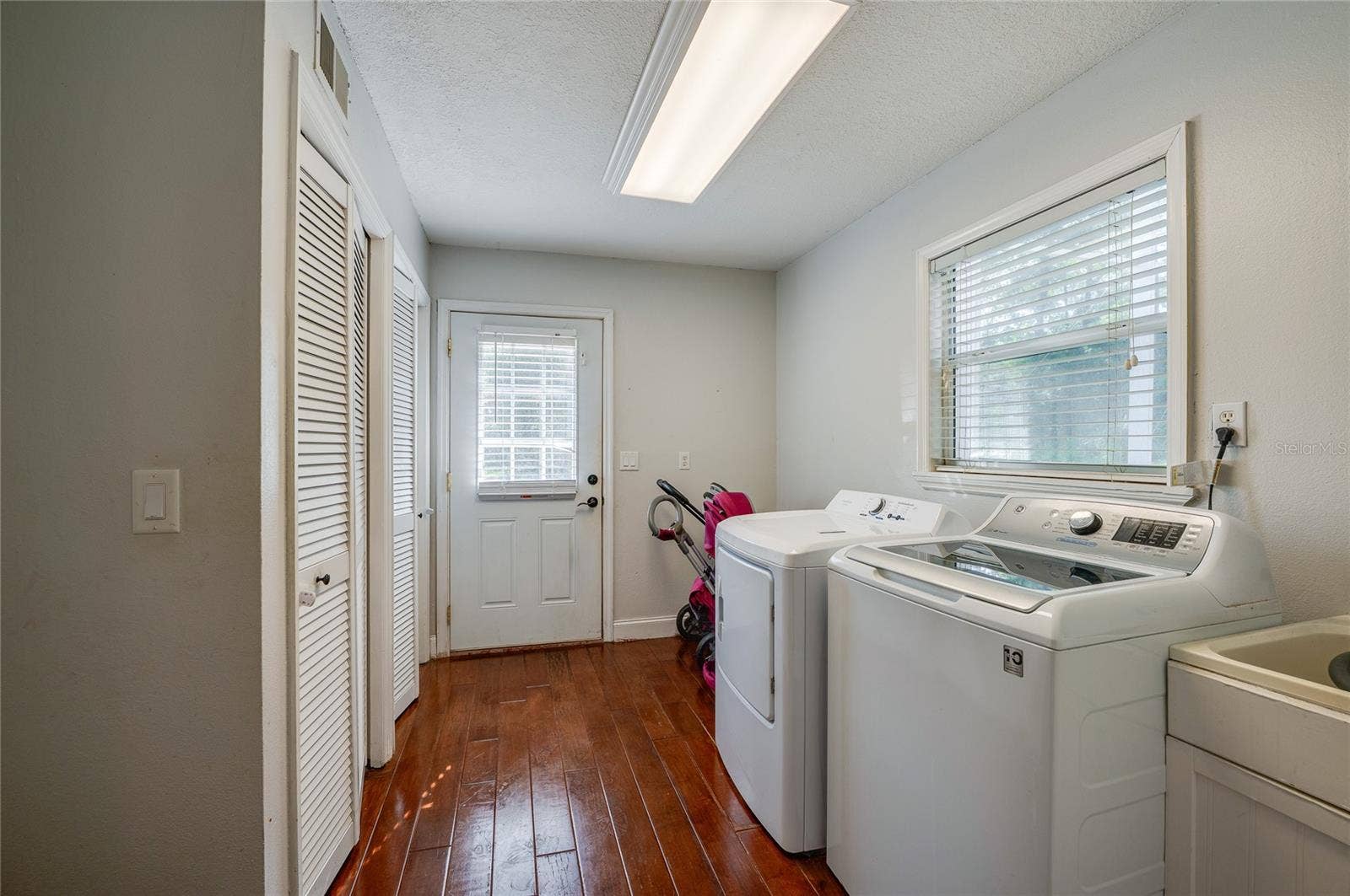 Convenient laundry room equipped with a washer, dryer, utility sink, louvered closet doors, and direct exterior door access.