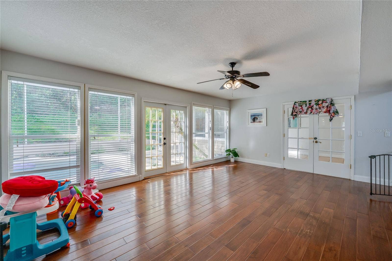 Open living area featuring rich laminate floors, a central ceiling fan, and multiple paned windows and glass doors opening to the outdoor pool patio.