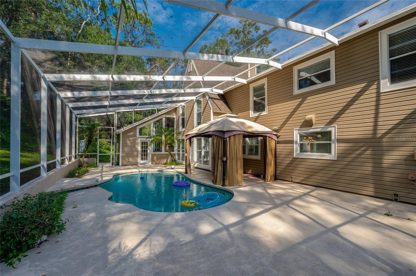 Spacious outdoor patio with a covered gazebo sitting alongside a sparkling, screened-in in-ground pool.