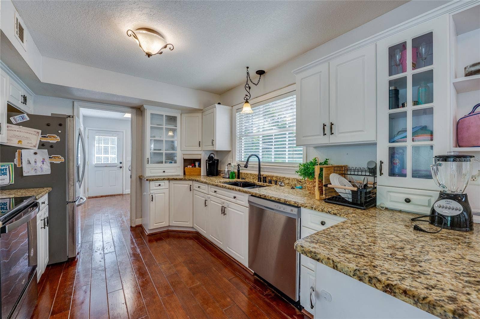 Bright, spacious kitchen showcasing white cabinetry, speckled granite countertops, stainless steel appliances, and rich laminate flooring.
