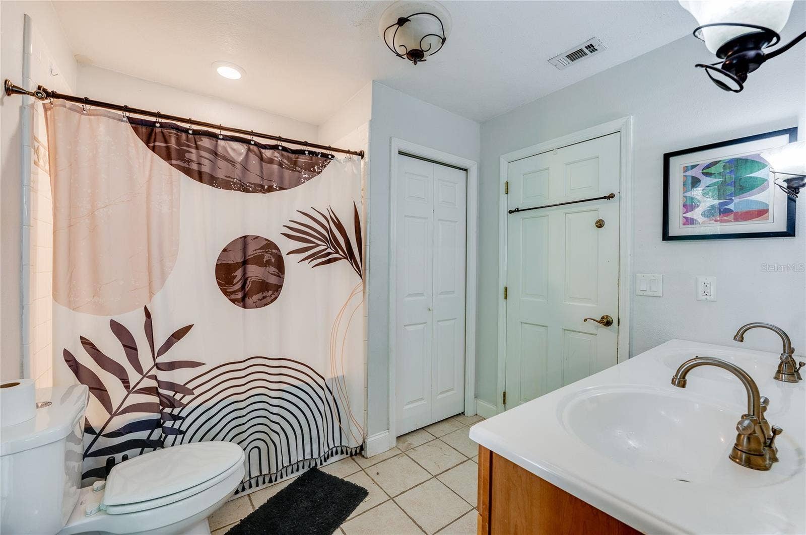 Full bathroom with tiled floors, a double-sink vanity with warm wood cabinetry, a tiled tub-shower combination, and a separate linen closet.