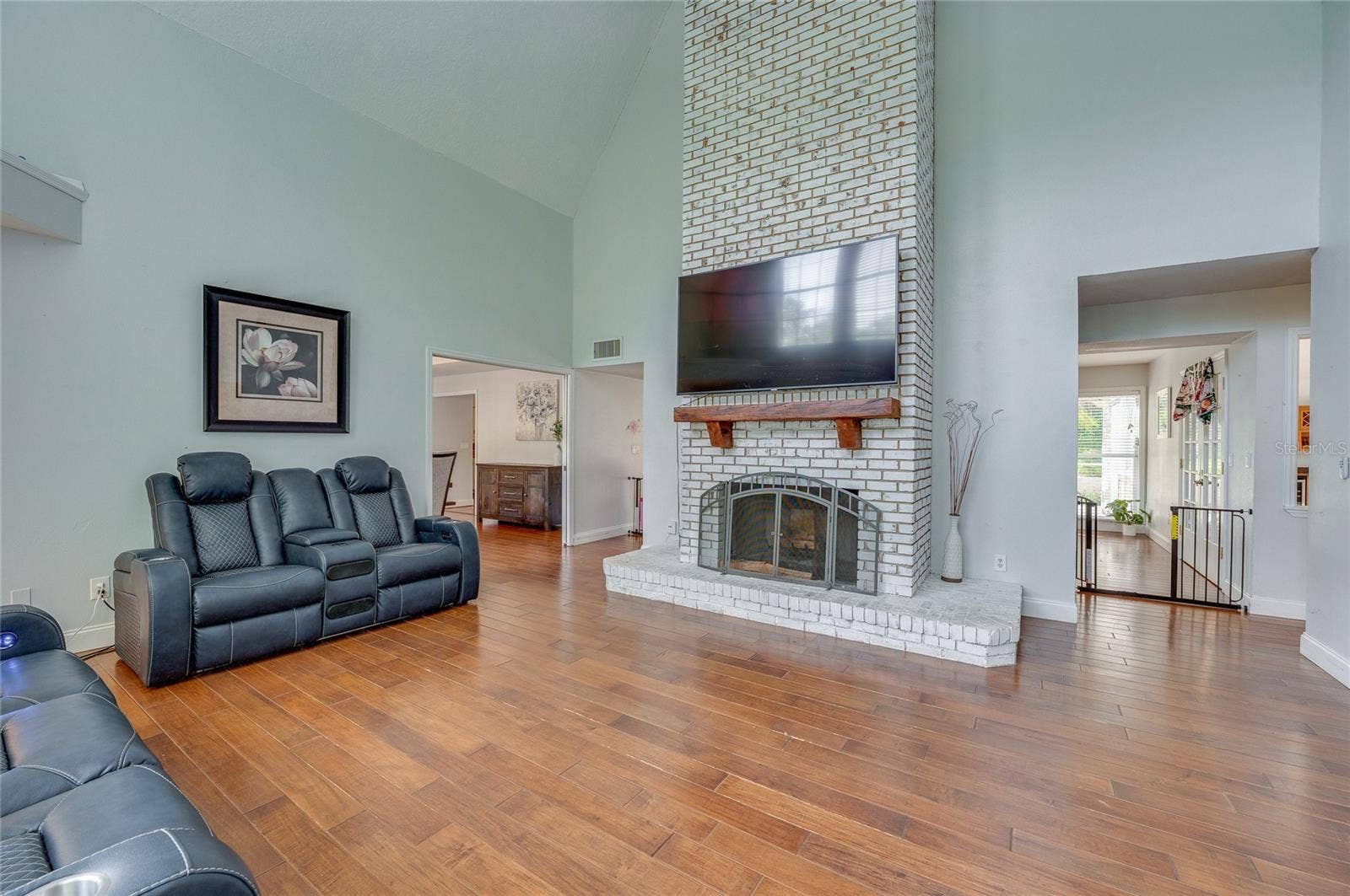 Soaring living room view centered around a floor-to-ceiling whitewashed brick fireplace with a rustic mantel and laminate flooring throughout.