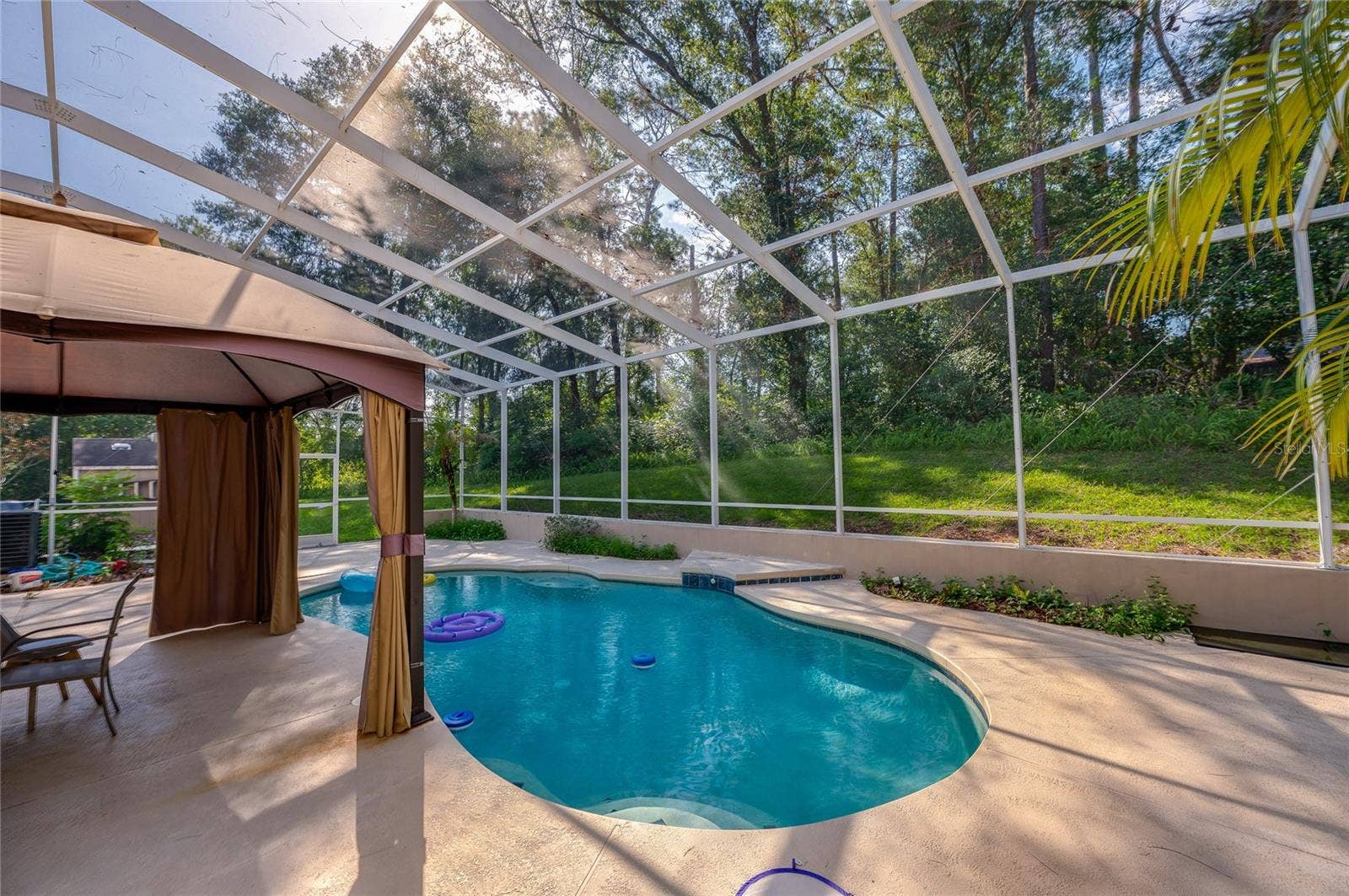 Screened-in patio enclosure sheltering a private in-ground swimming pool surrounded by a spacious concrete deck and mature trees.