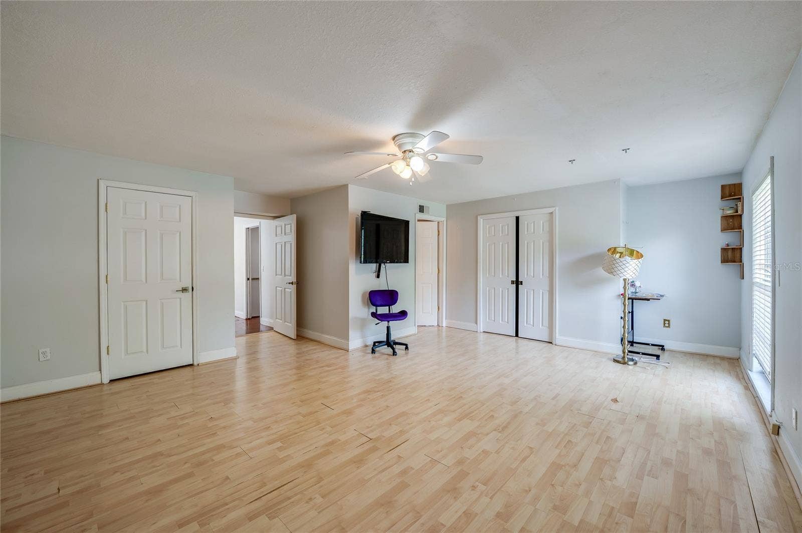 Wide interior shot of a spacious room with light laminate flooring, a ceiling fan, and multiple white panel doors.