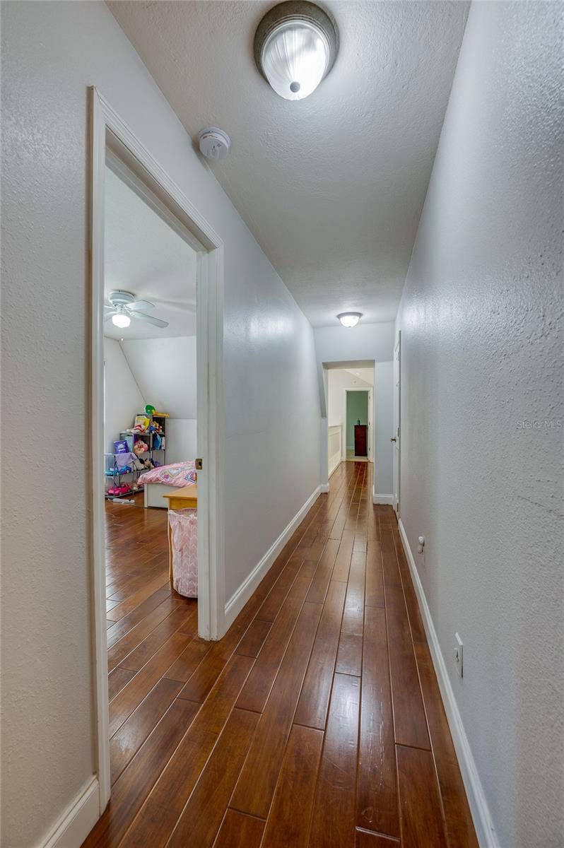 Long interior hallway showcasing polished laminate flooring, recessed ceiling lights, and white trim throughout.