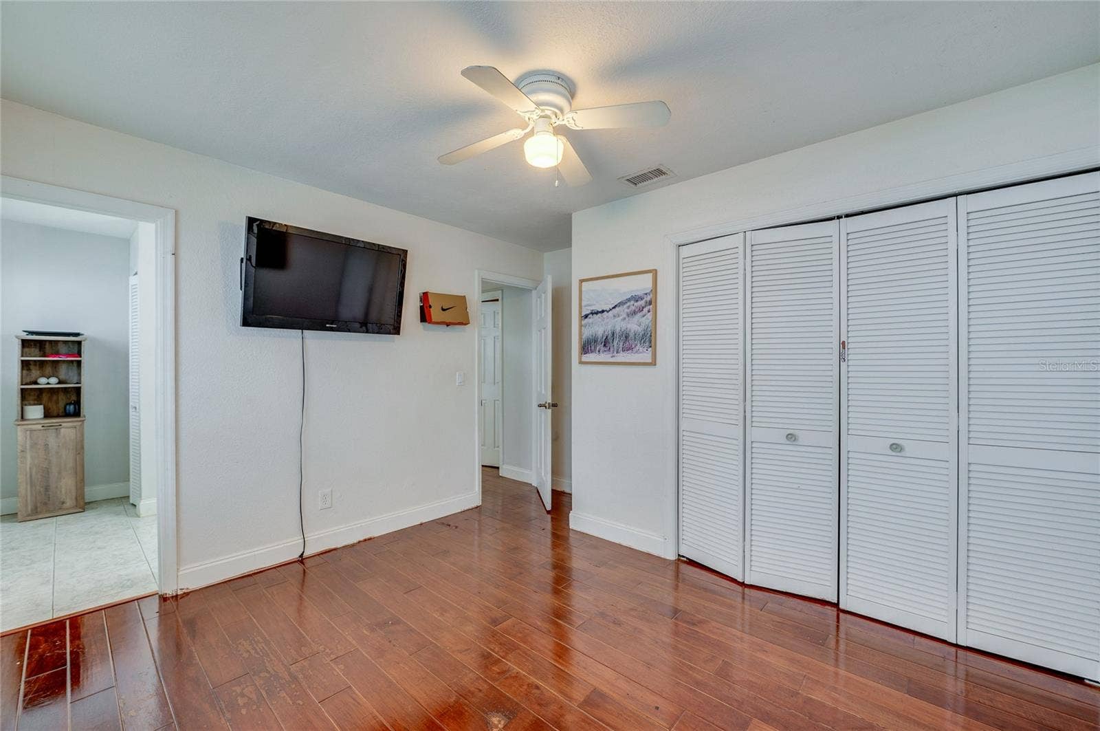 Bright bedroom area highlighting rich dark laminate flooring, crisp white walls, a central ceiling fan, and closet doors.