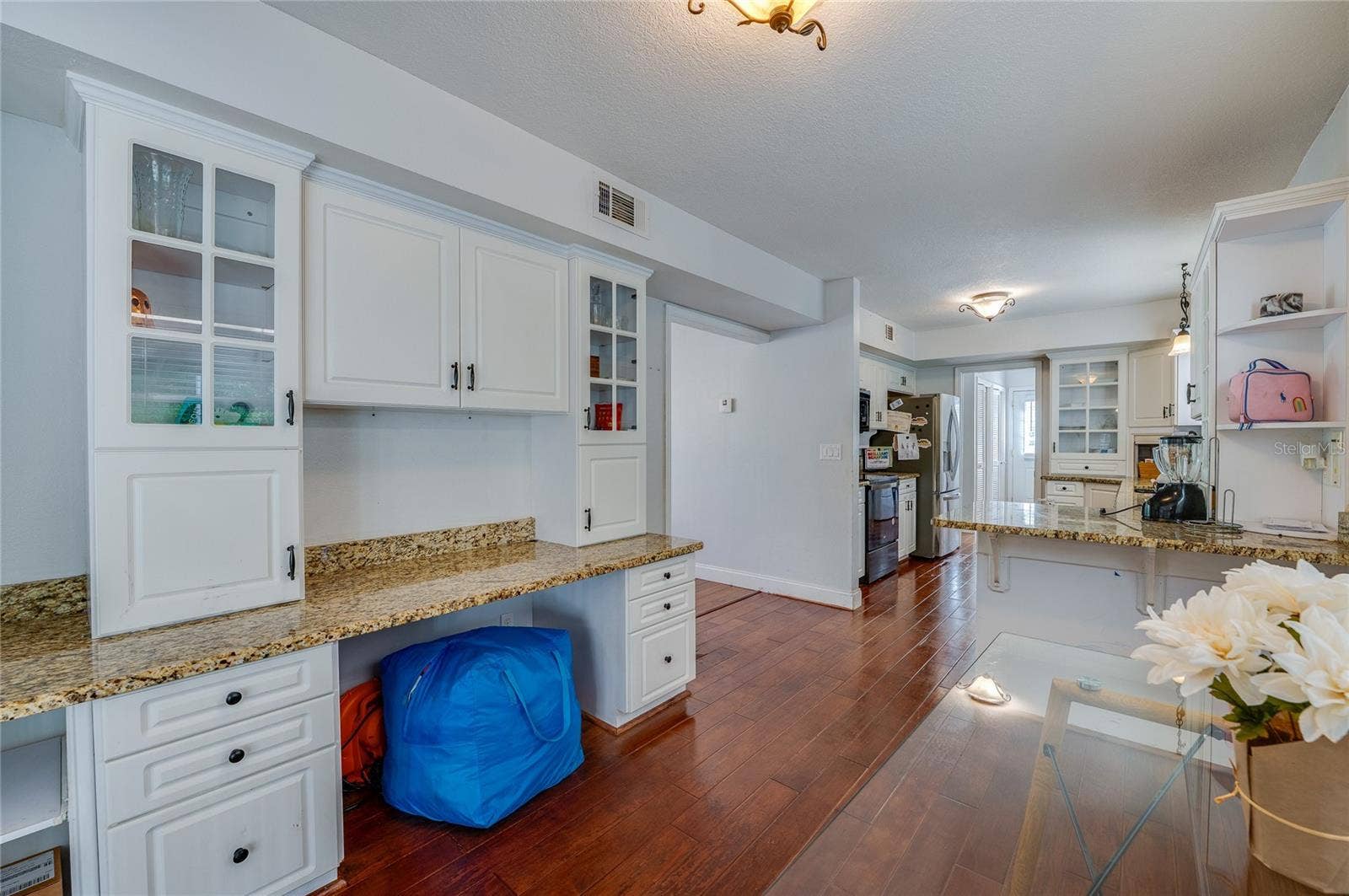 Bright kitchen prep space featuring white cabinetry with glass-front uppers, granite countertops, and seamless laminate flooring leading to adjacent rooms.